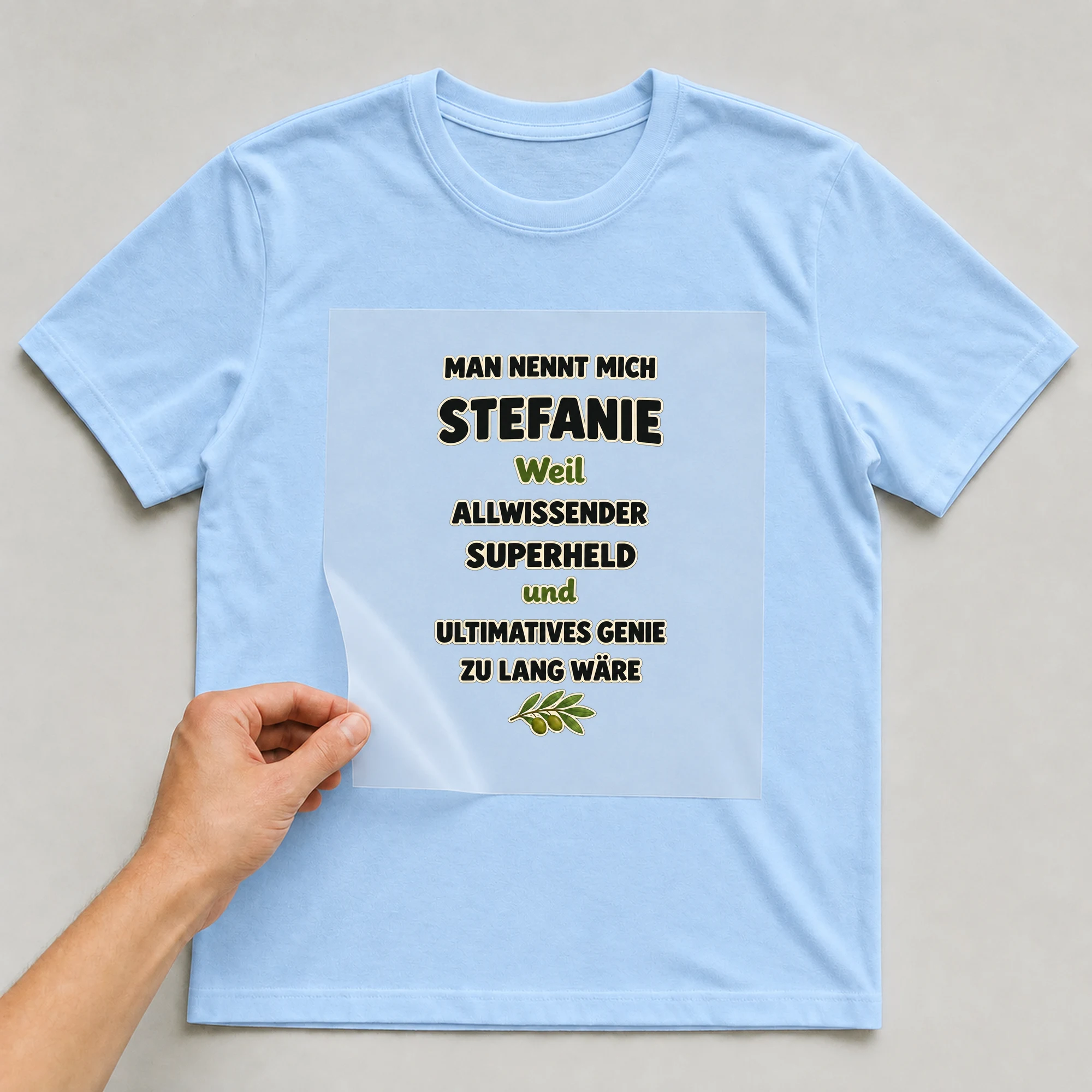 Bügelbild „Man nennt mich Stefanie weil allwissender Superheld und ultimatives Genie zu“ auf babyblauem T-Shirt, Folie wird aufgelegt