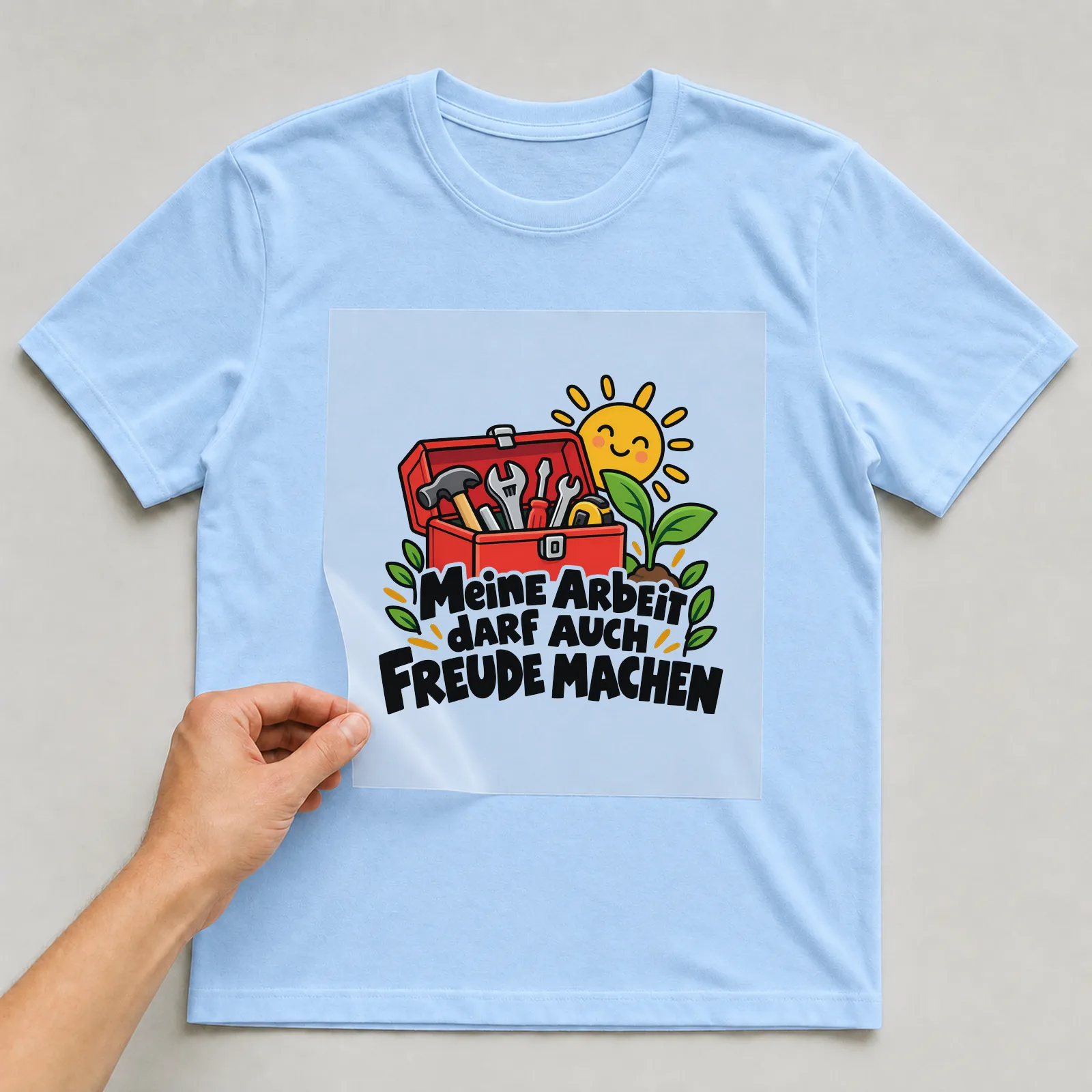 Bügelbild „Meine Arbeit DARF AUCH FREUDE MACHEN“ auf hellblauem T-Shirt, Folie wird aufgelegt