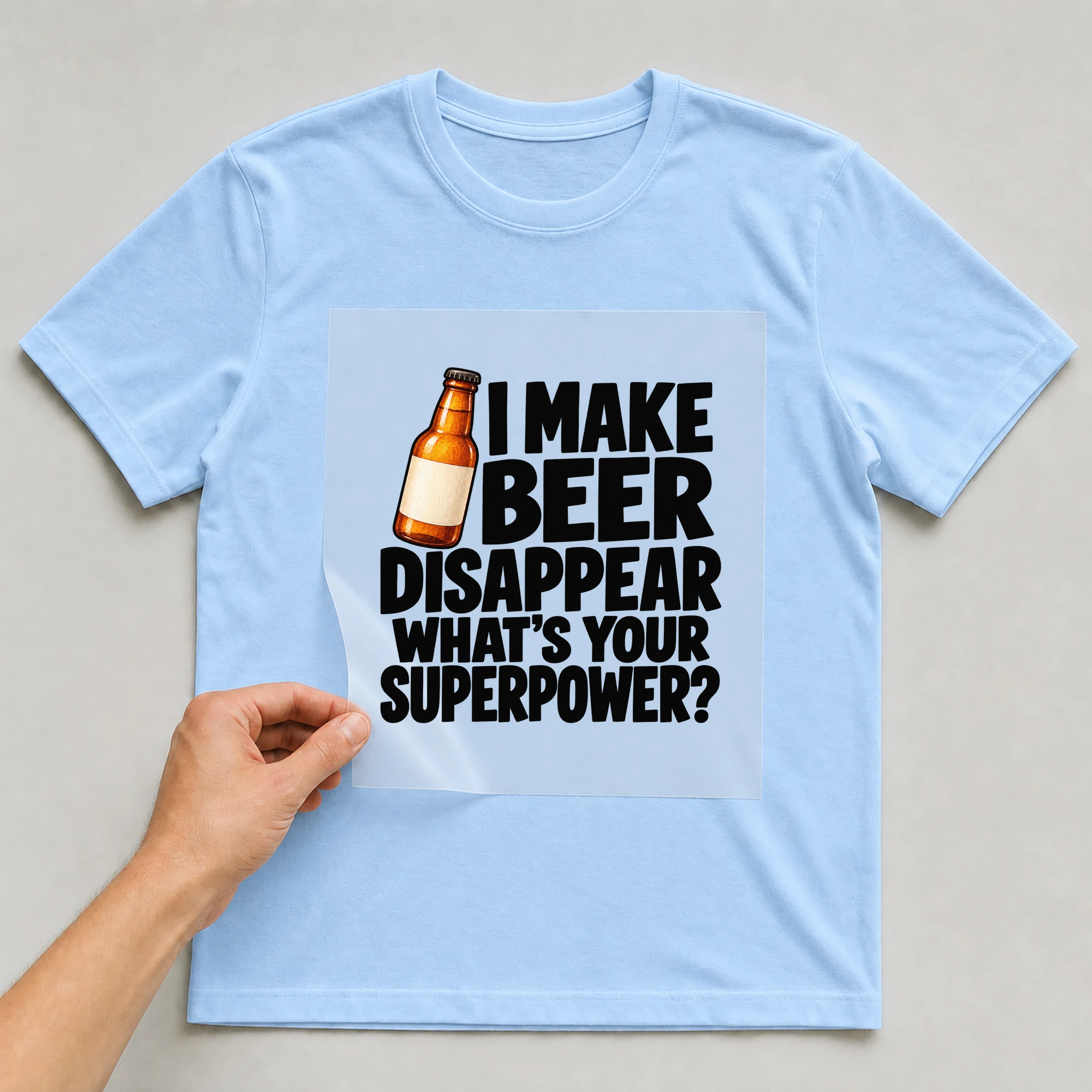 Bügelbild „I Make Beer Disappear What's Your Superpower?“ auf babyblauem T-Shirt, Folie wird aufgelegt