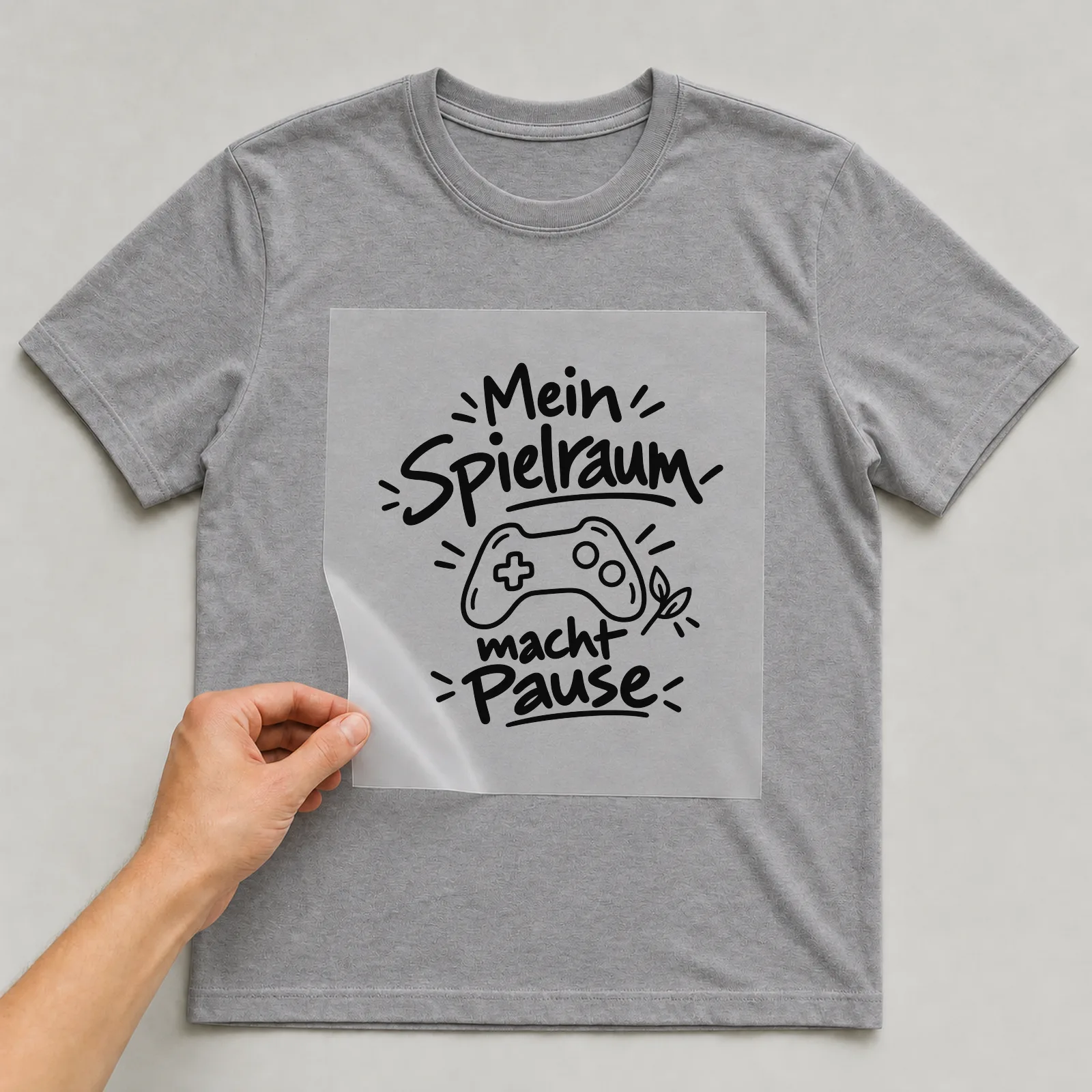 Bügelbild „Mein Spielraum macht Pause“ auf grauem T-Shirt, Folie wird aufgelegt