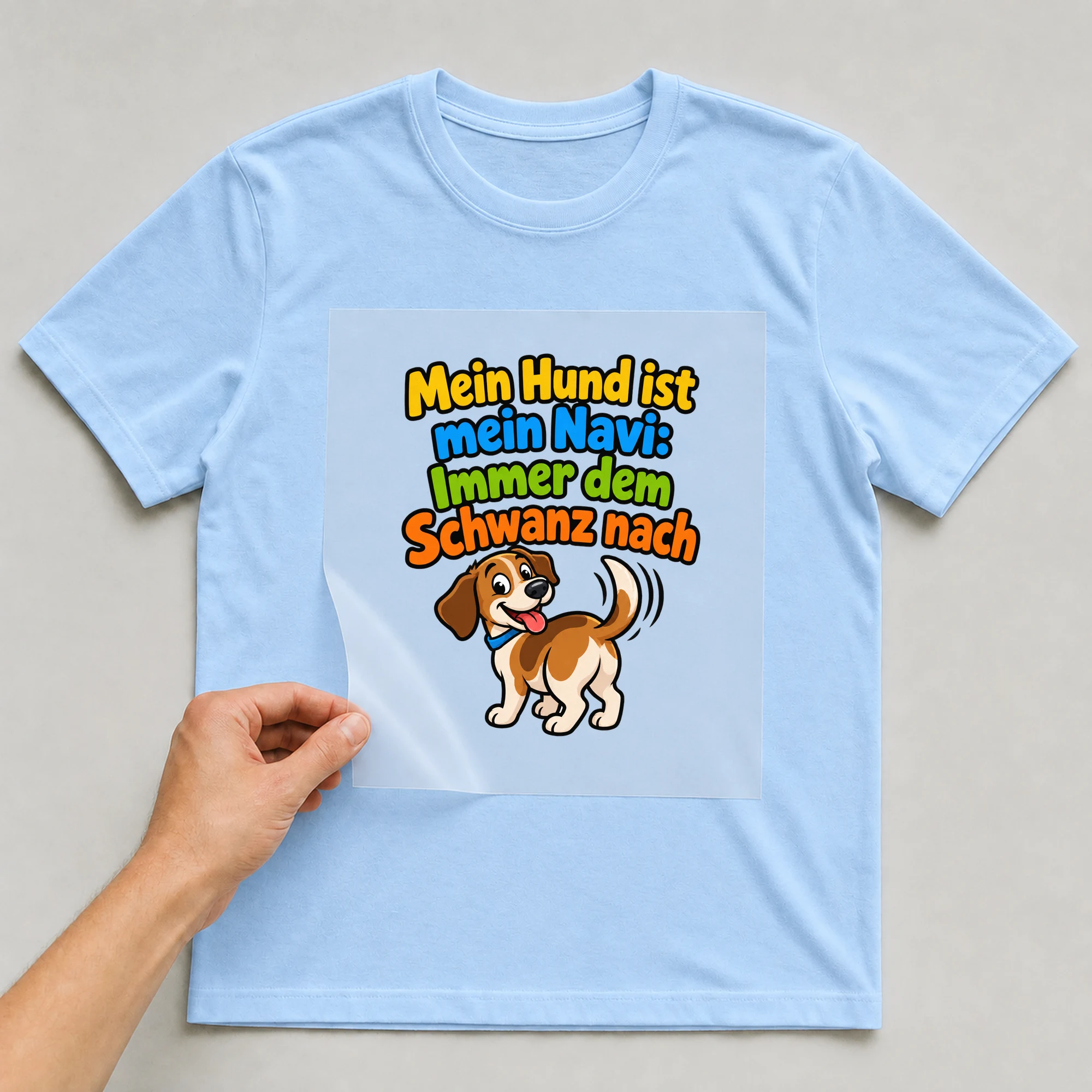 Bügelbild „Mein Hund ist mein Navi: Immer dem Schwanz nach“ auf babyblauem T-Shirt, Folie wird aufgelegt