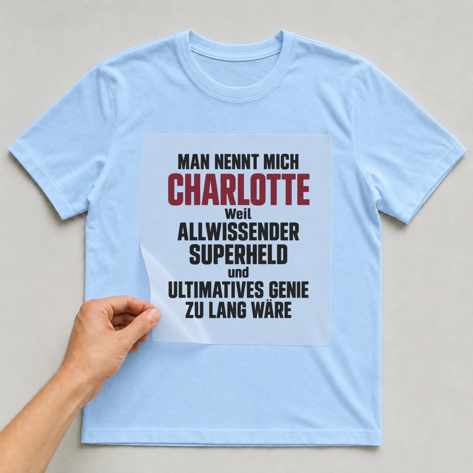Bügelbild „Man nennt mich Charlotte weil allwissender Superheld und ultimatives Genie zu“ auf babyblauem T-Shirt, Folie wird aufgelegt