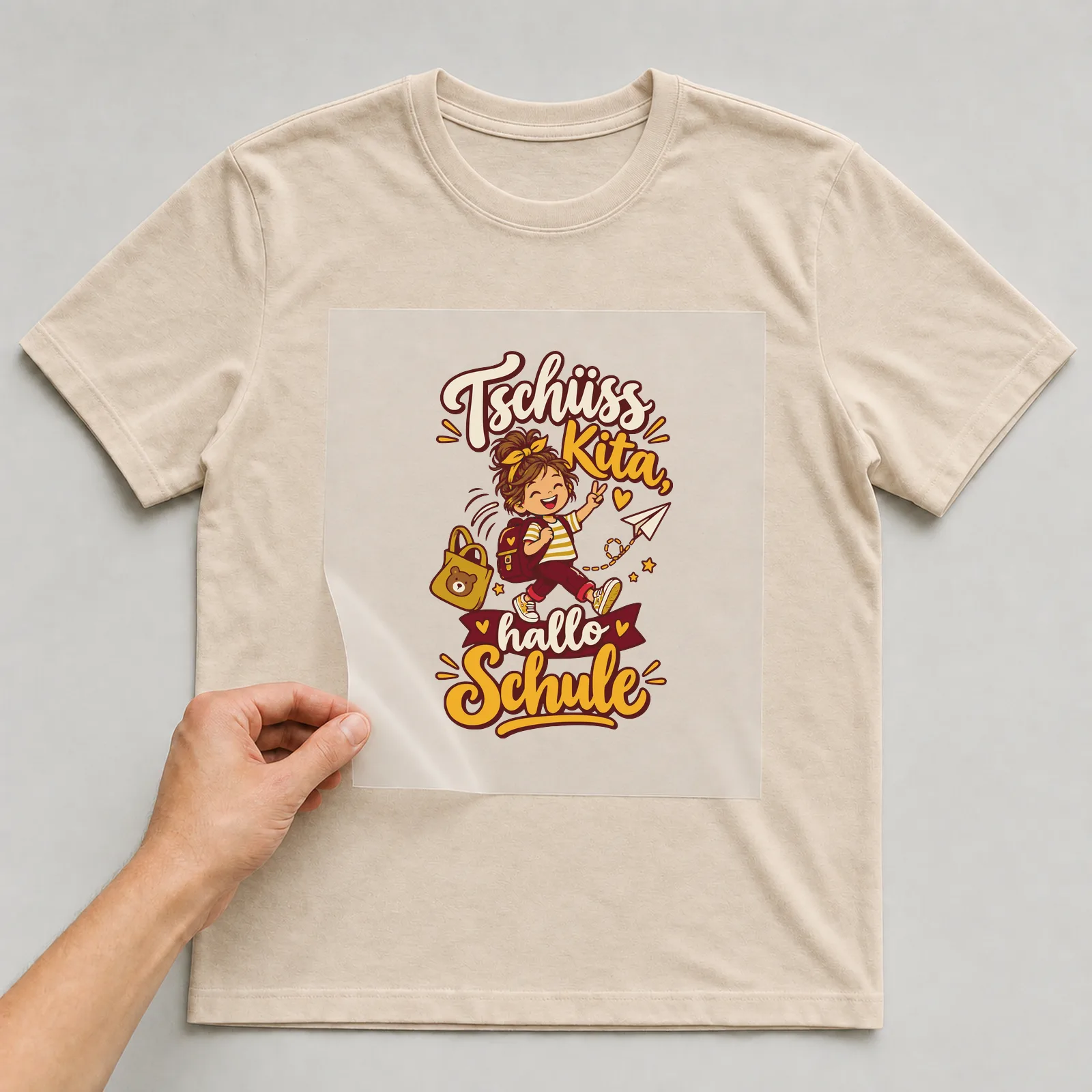 Bügelbild Tschüss Kita, hallo Schule auf beigem T-Shirt, Folie wird aufgelegt