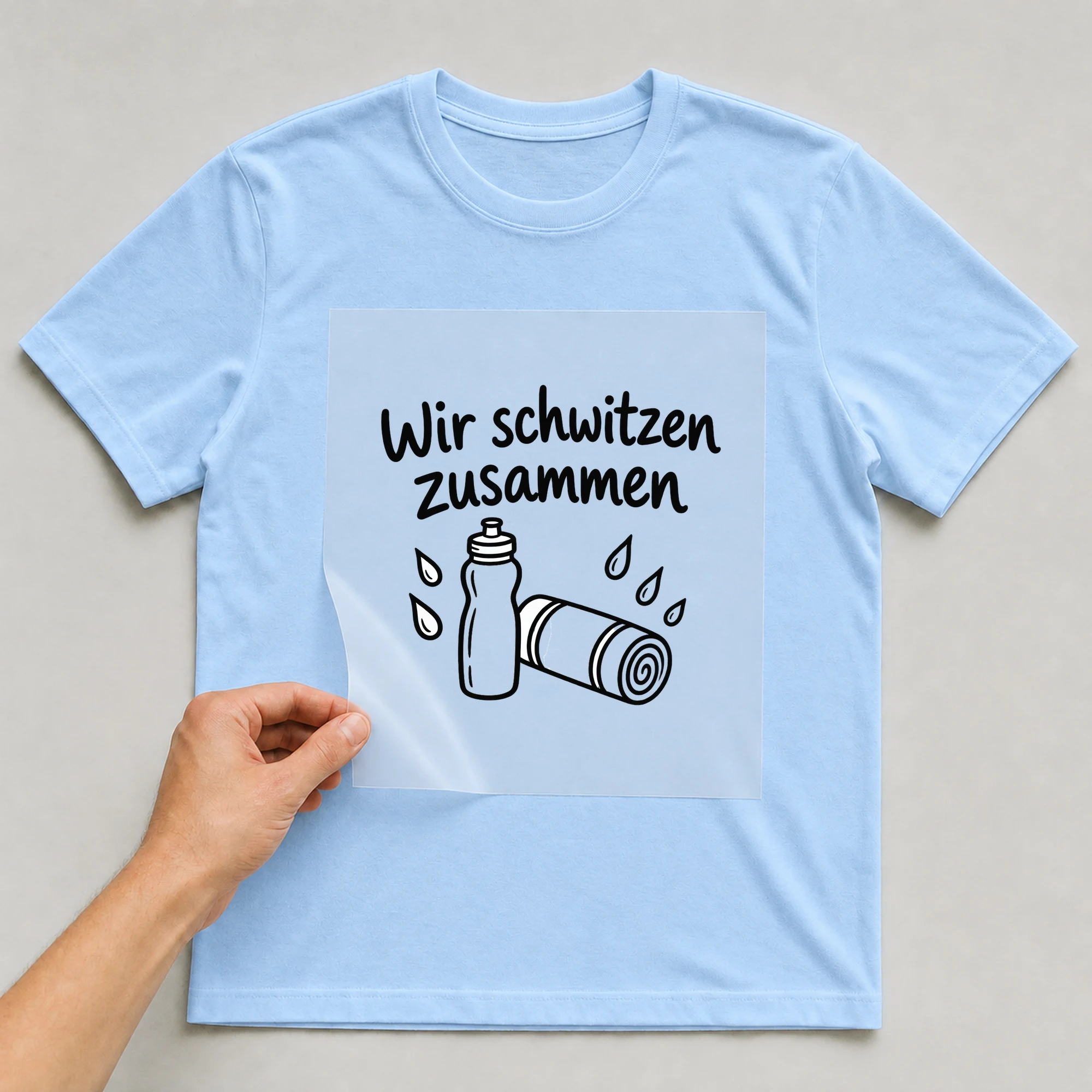 Bügelbild „Wir schwitzen zusammen“ auf babyblauem T-Shirt, Folie wird aufgelegt