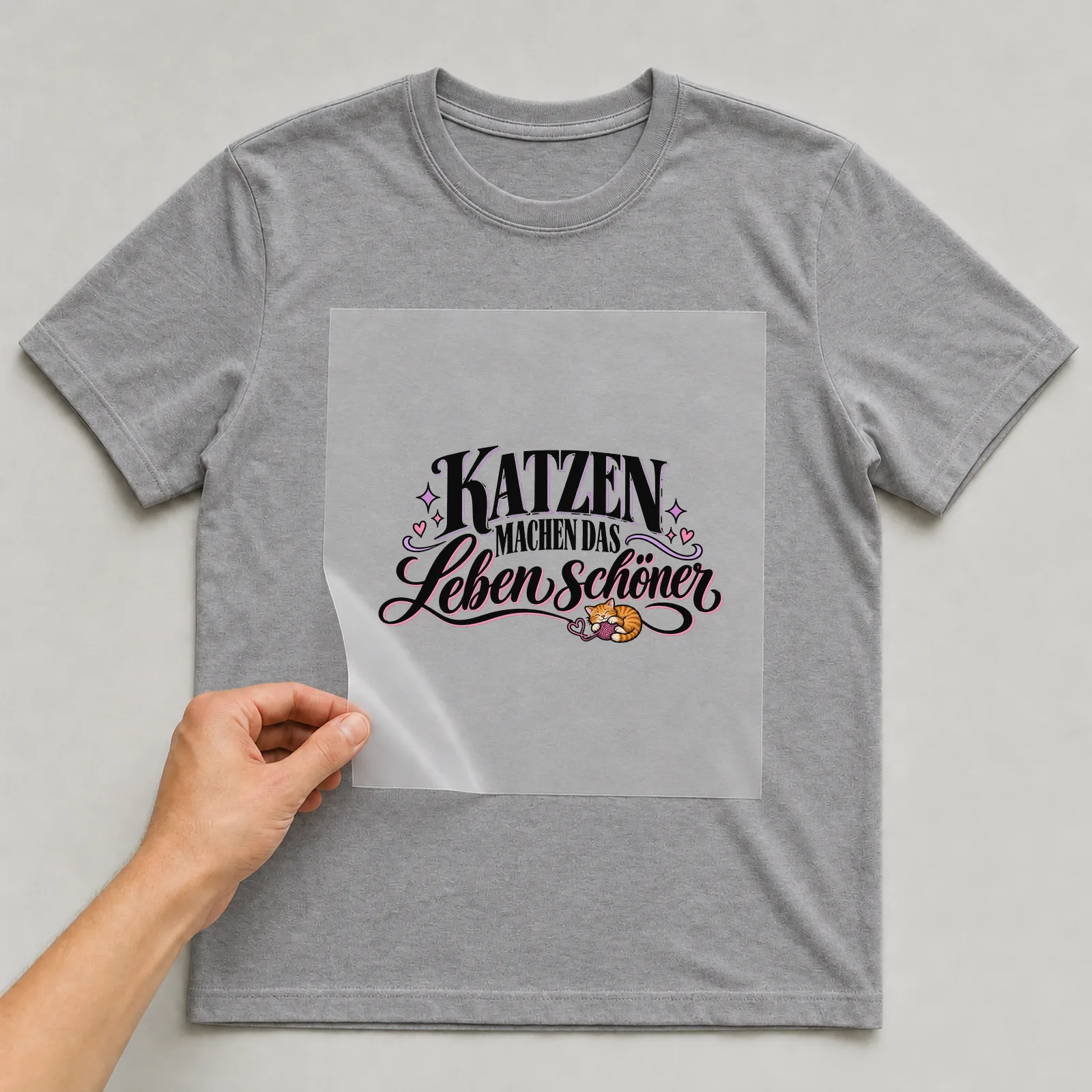 Bügelbild „Katzen machen das Leben schöner“ auf grauem T-Shirt, Folie wird aufgelegt