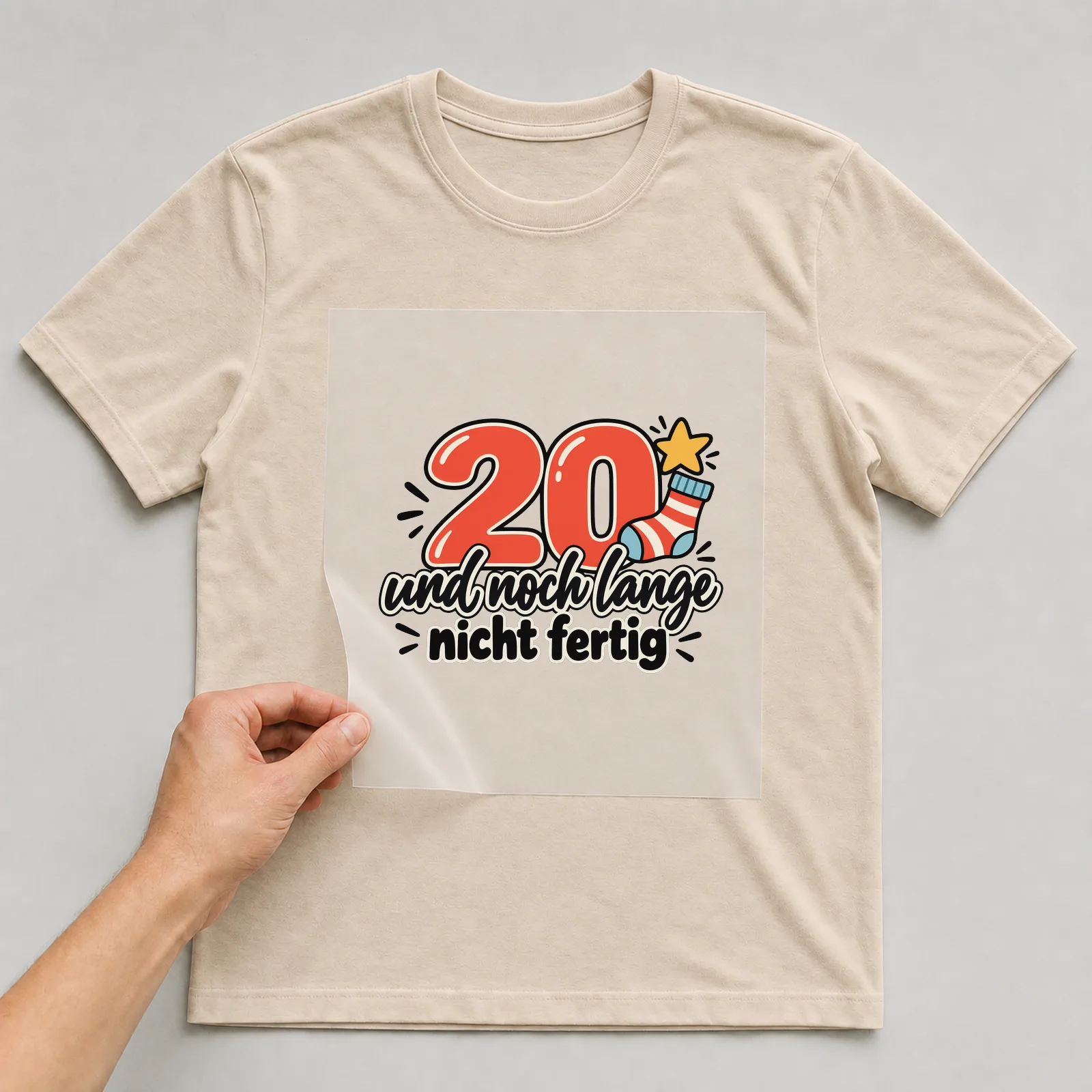 Bügelbild „20 und noch lange nicht fertig“ auf beigem T-Shirt, Folie wird aufgelegt