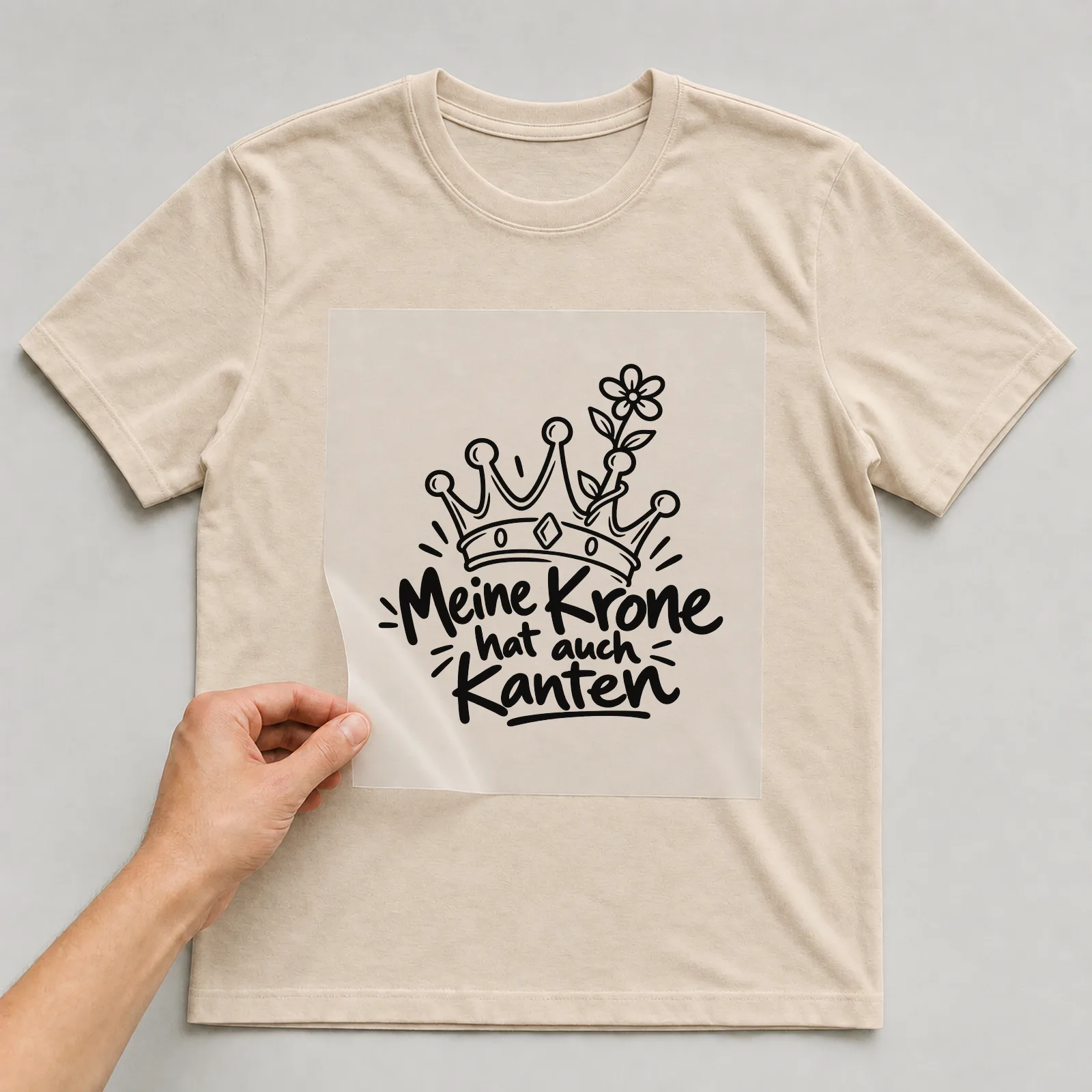 Bügelbild „Meine Krone hat auch Kanten“ auf beigem T-Shirt, Folie wird aufgelegt