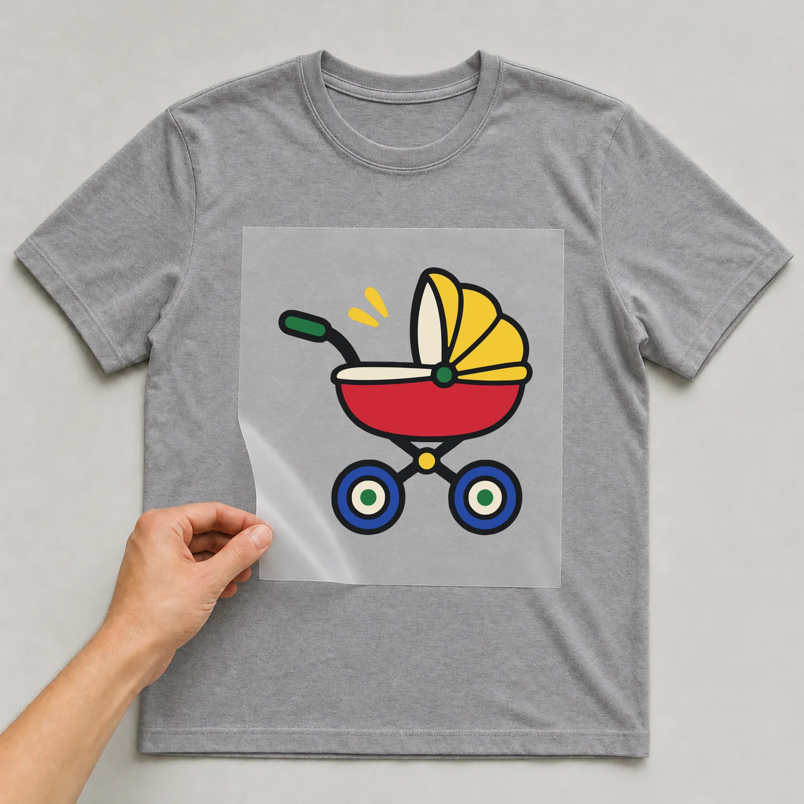 Bügelbild Kinderwagen im Comic-Stil auf grauem T-Shirt, Folie wird aufgelegt