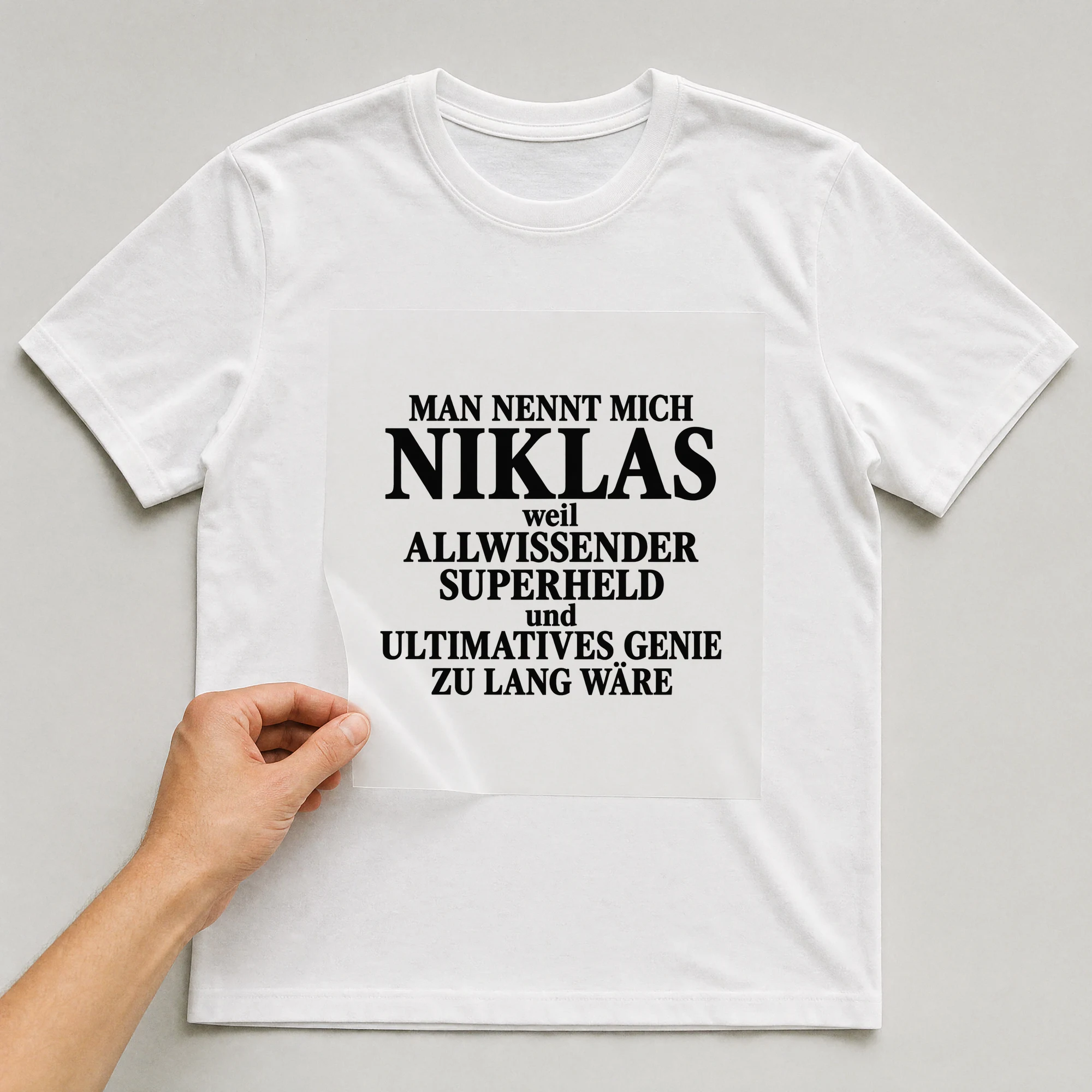 Bügelbild „Man nennt mich Niklas weil allwissender Superheld und ultimatives Genie zu“ auf weißem T-Shirt, Folie wird aufgelegt