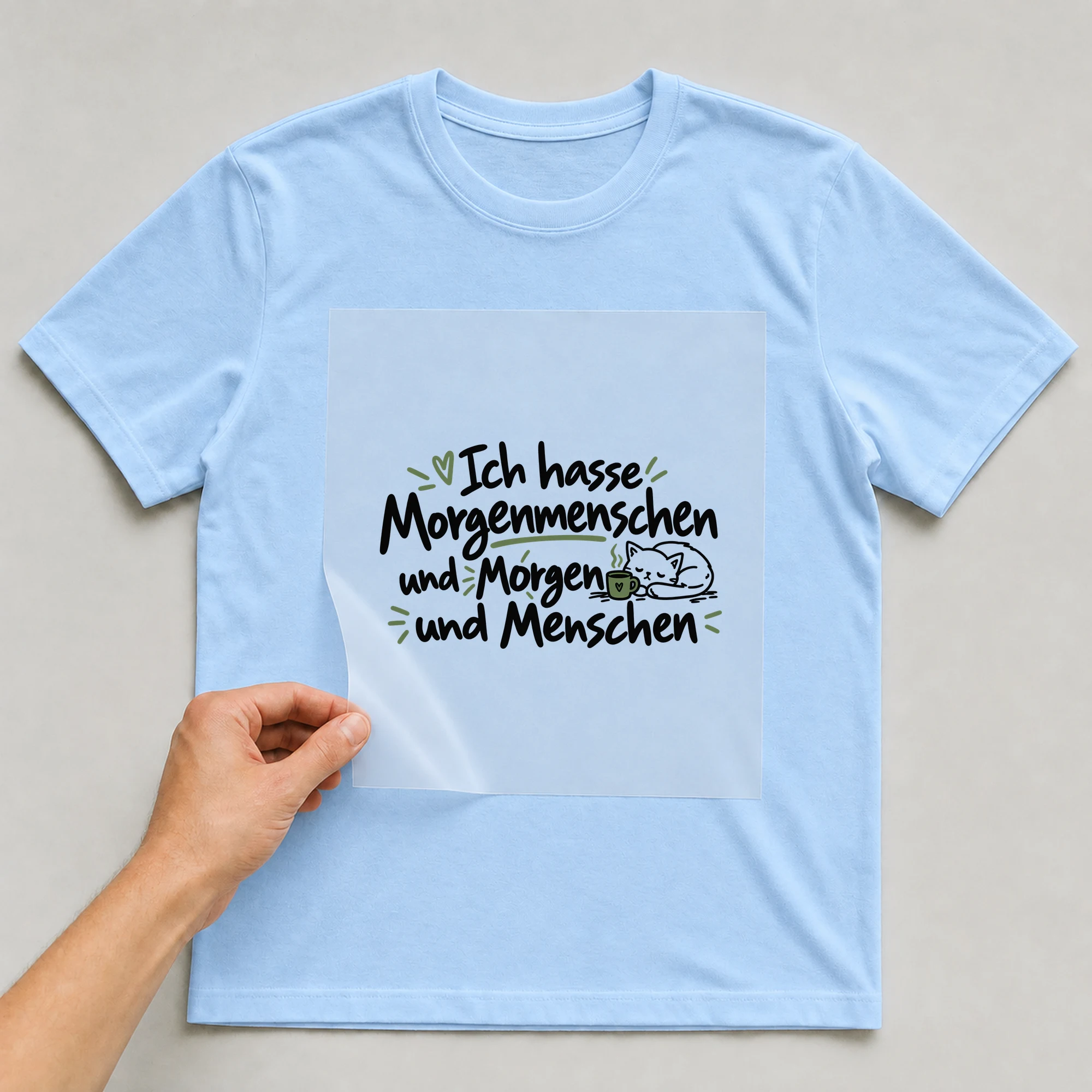 Bügelbild „Ich hasse Morgenmenschen und Morgen und Menschen“ auf babyblauem T-Shirt, Folie wird aufgelegt