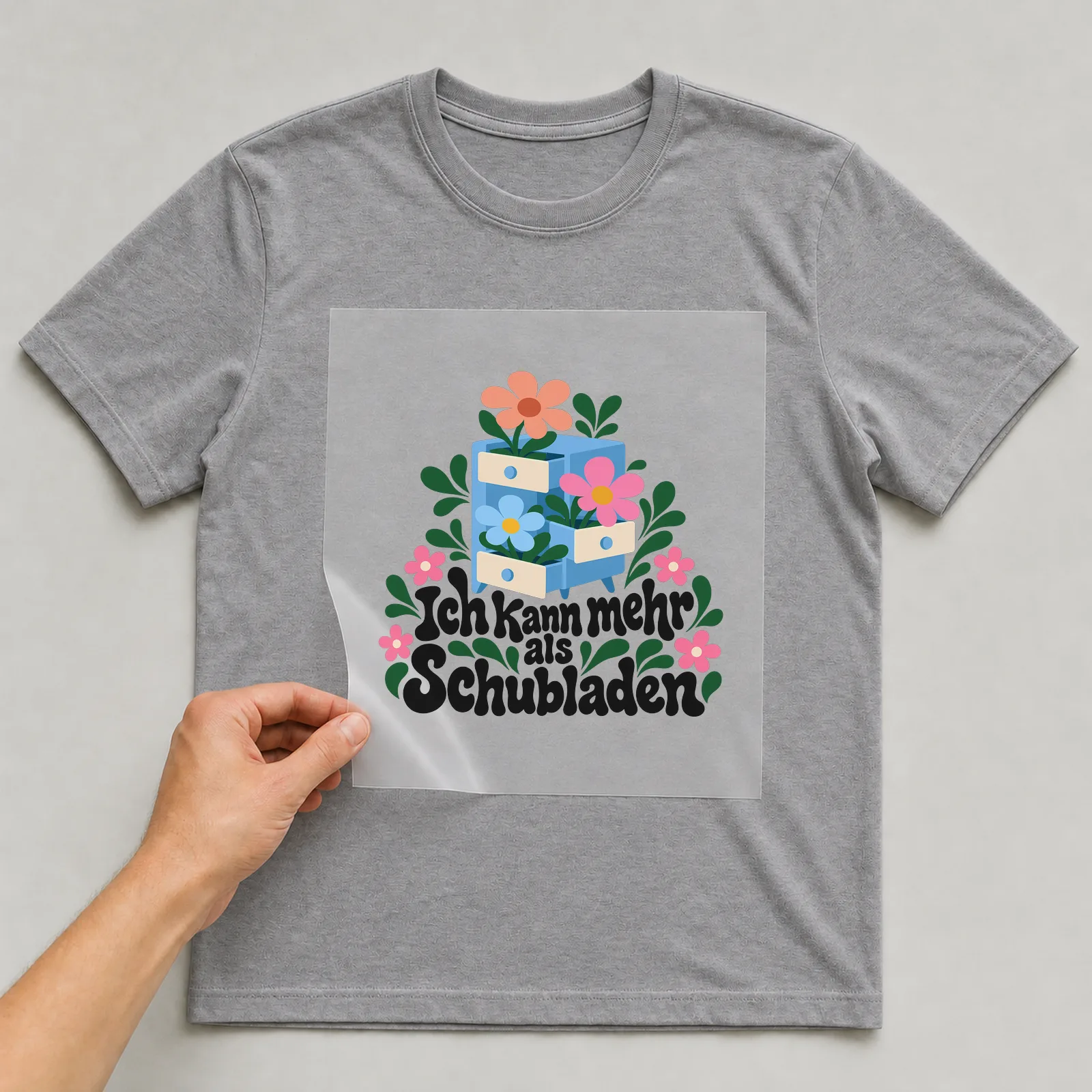 Bügelbild „Ich kann mehr als Schubladen“ auf grauem T-Shirt, Folie wird aufgelegt