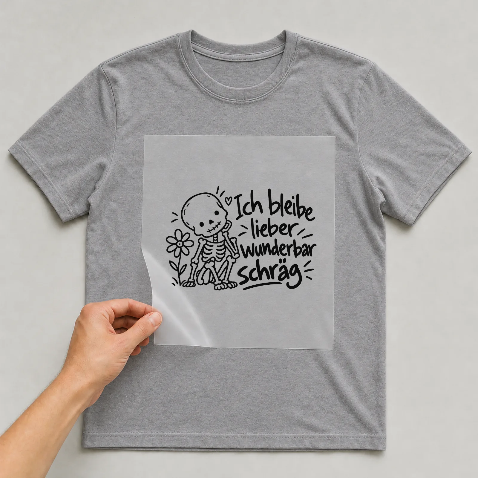 Bügelbild „Ich bleibe lieber wunderbar schräg“ auf grauem T-Shirt, Folie wird aufgelegt