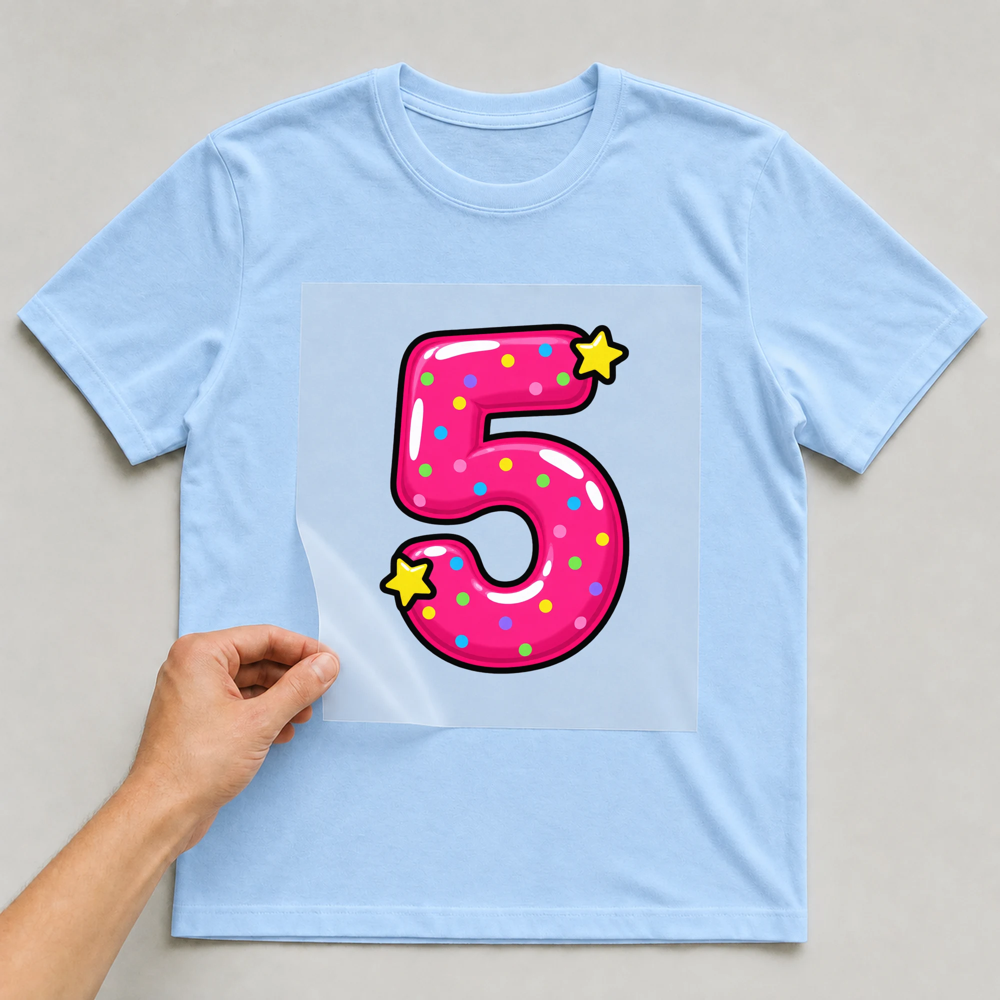 Bügelbild „Zahl 5 im Comic-Ballon-Stil“ auf babyblauem T-Shirt, Folie wird aufgelegt