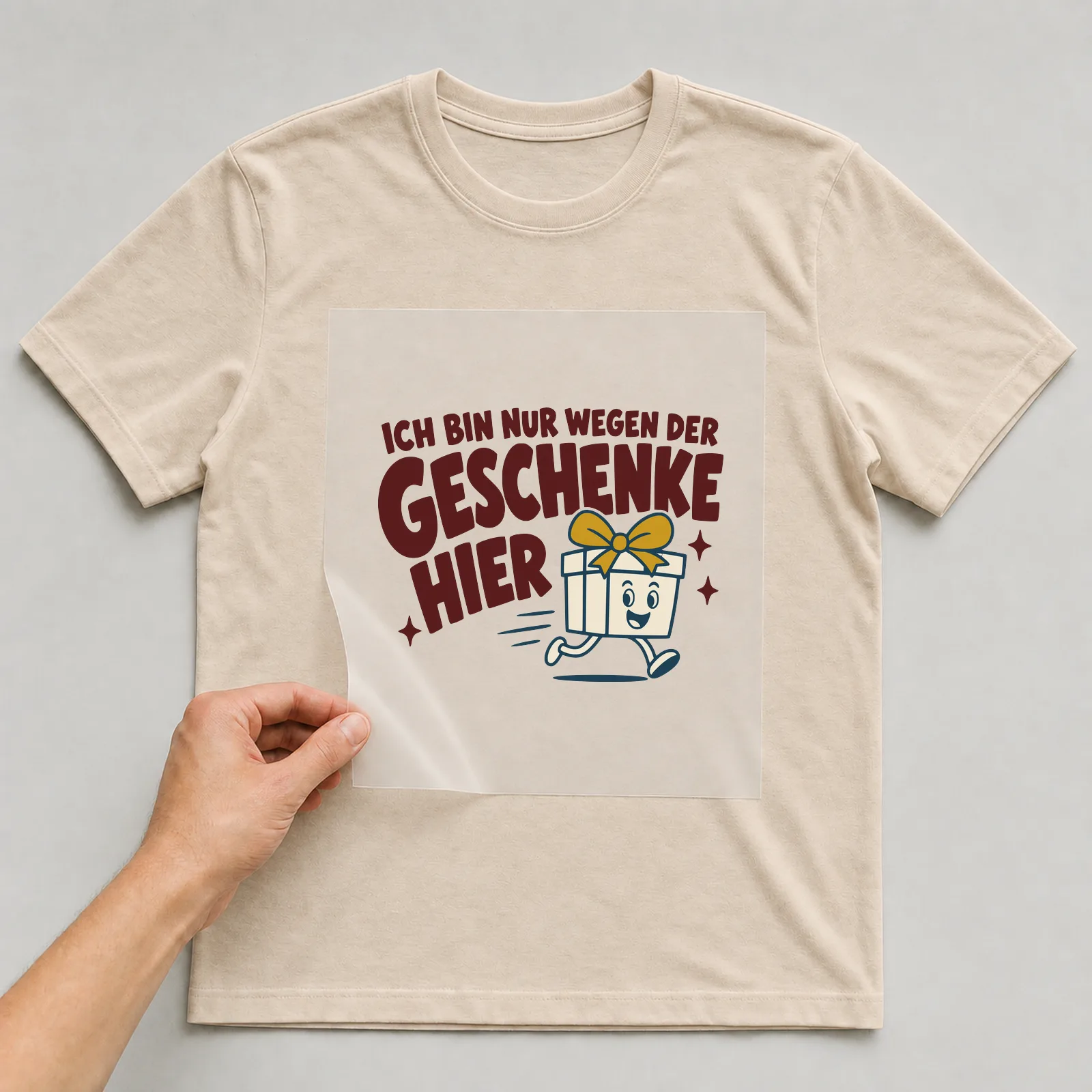 Bügelbild Ich bin nur wegen der Geschenke hier auf beigem T-Shirt, Folie wird aufgelegt