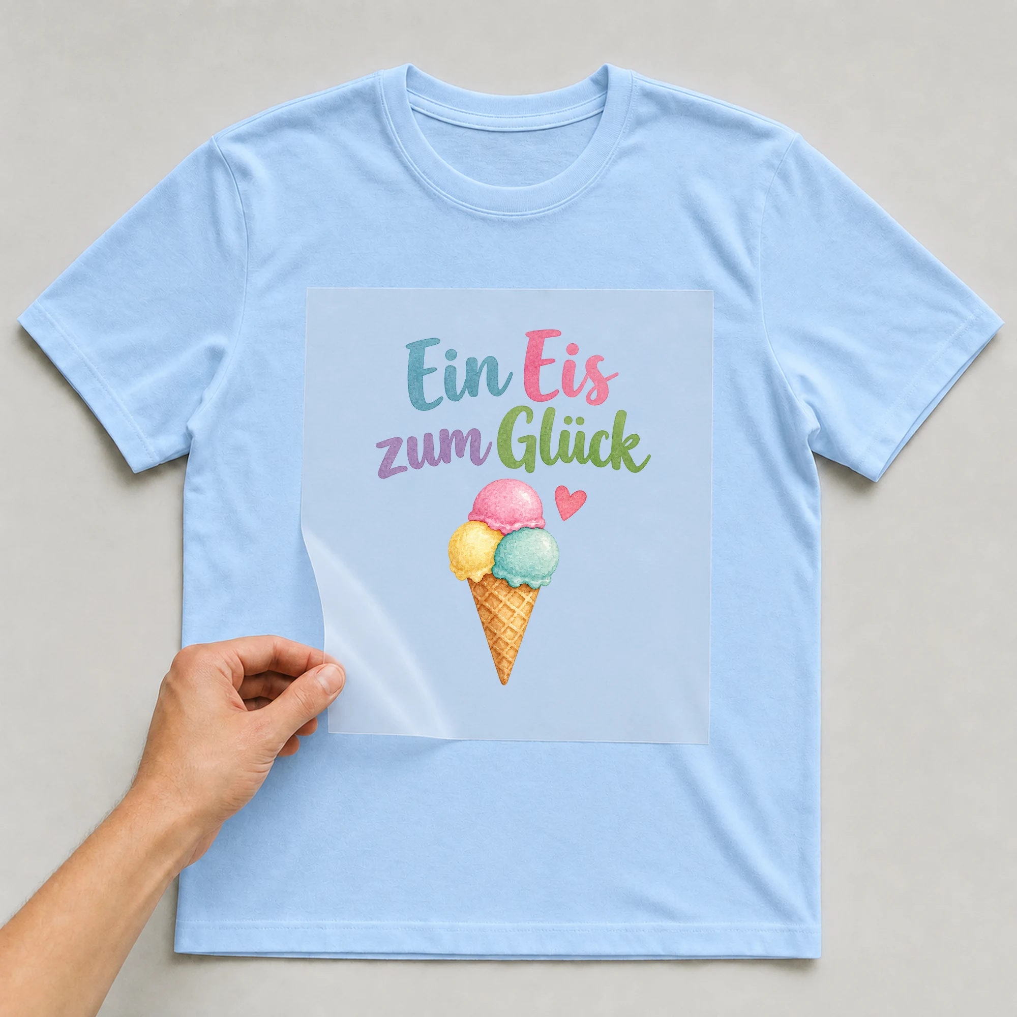 Bügelbild „Ein Eis zum Glück“ auf babyblauem T-Shirt, Folie wird aufgelegt