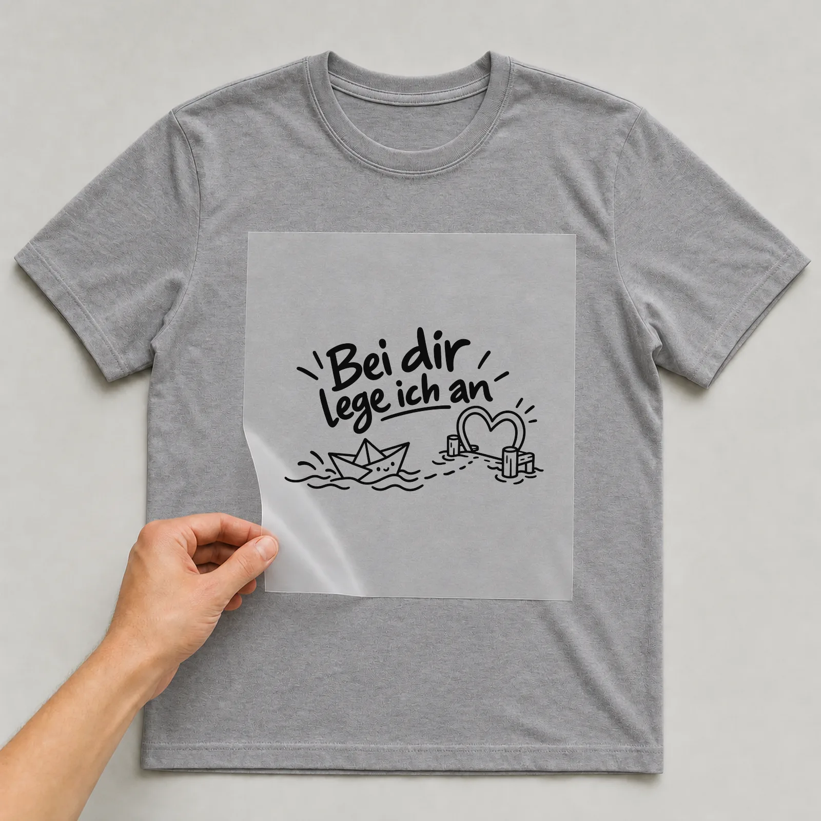 Bügelbild „Bei dir lege ich an“ auf grauem T-Shirt, Folie wird aufgelegt