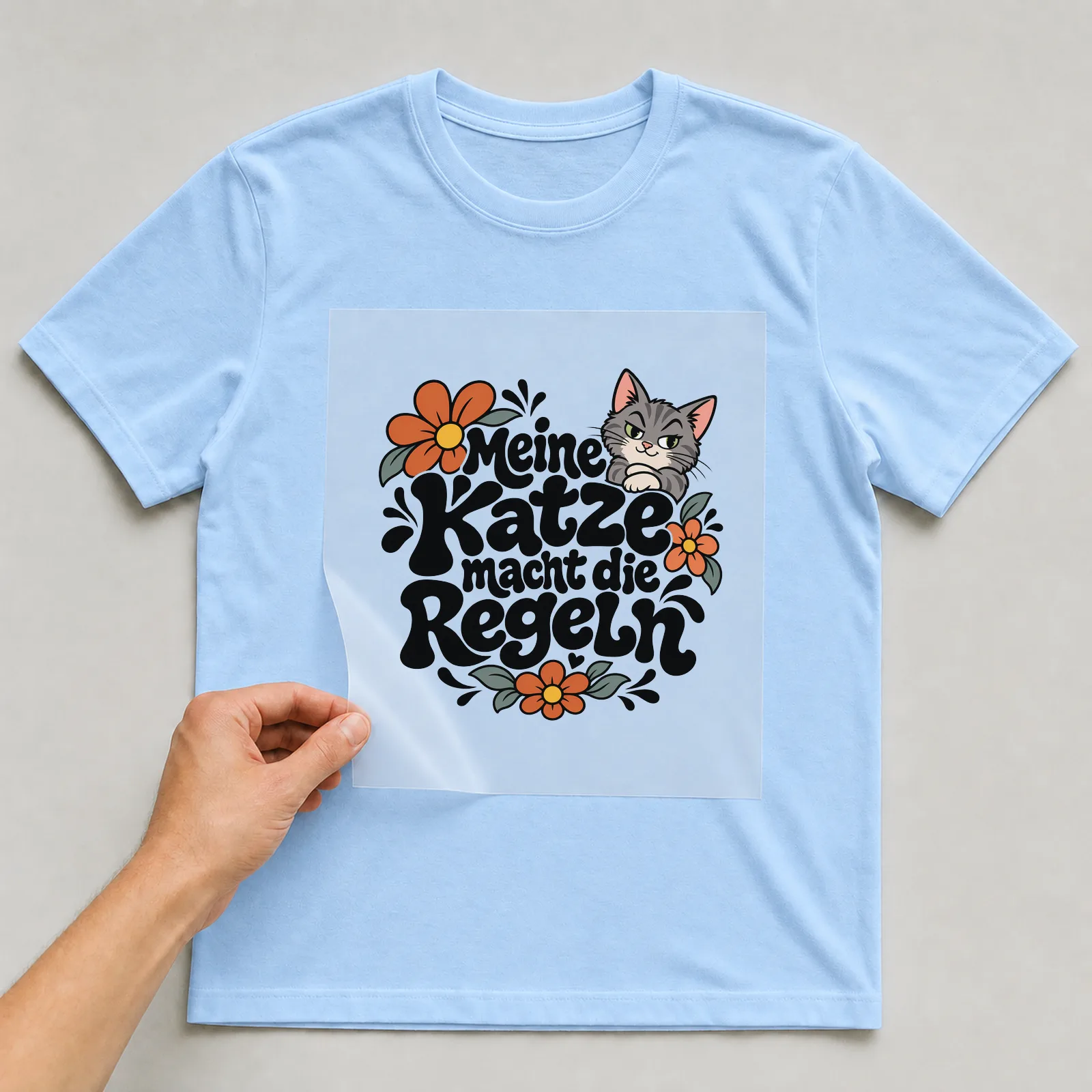 Bügelbild „Meine Katze macht die Regeln“ auf hellblauem T-Shirt, Folie wird aufgelegt