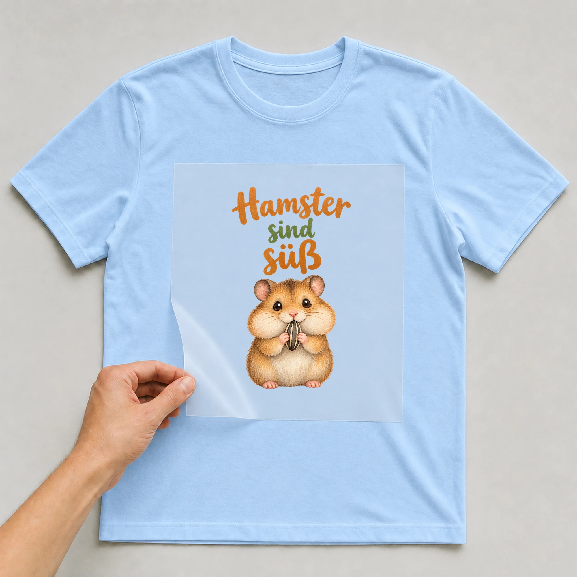 Bügelbild „Hamster sind süß“ auf babyblauem T-Shirt, Folie wird aufgelegt