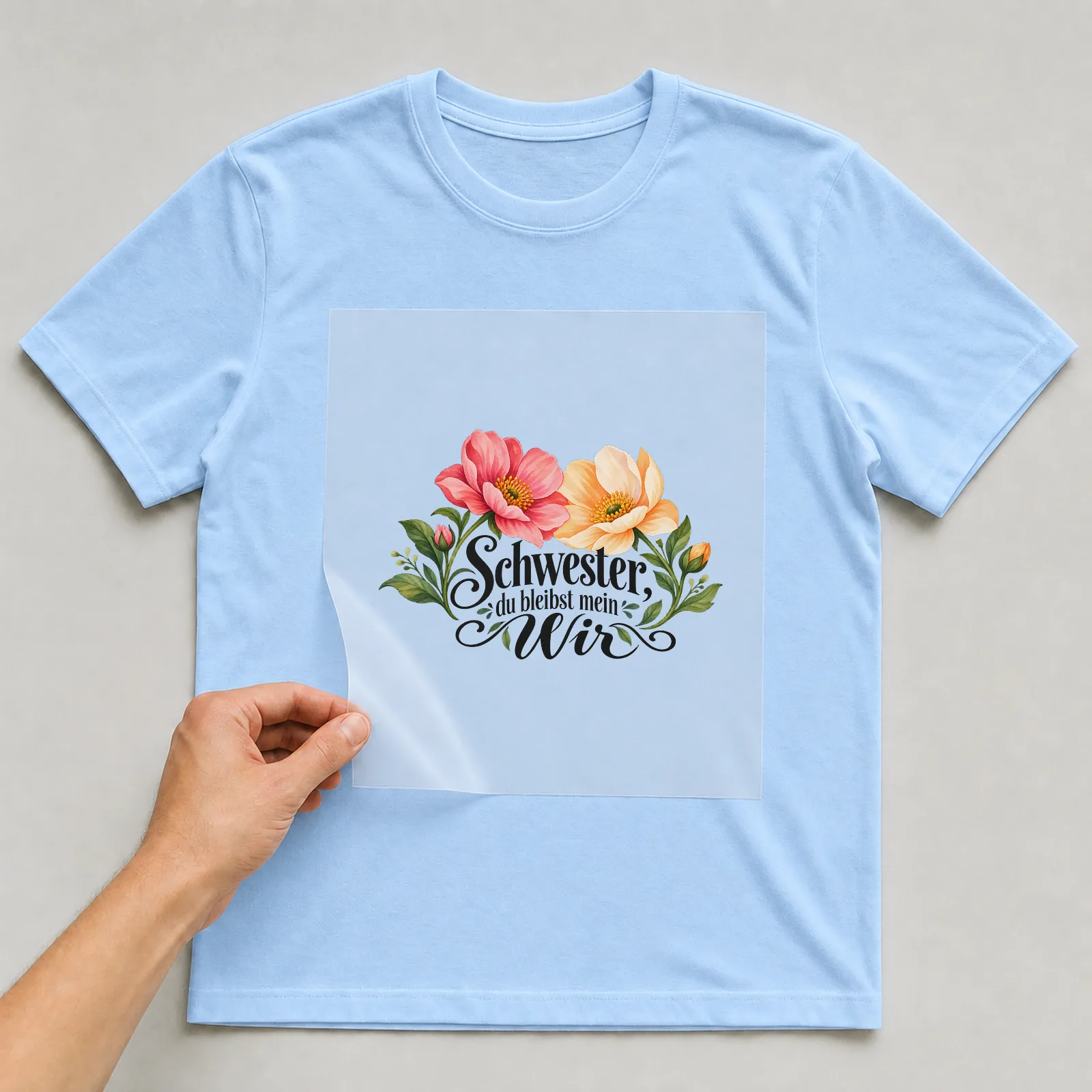 Bügelbild „Schwester, du bleibst mein Wir“ auf hellblauem T-Shirt, Folie wird aufgelegt