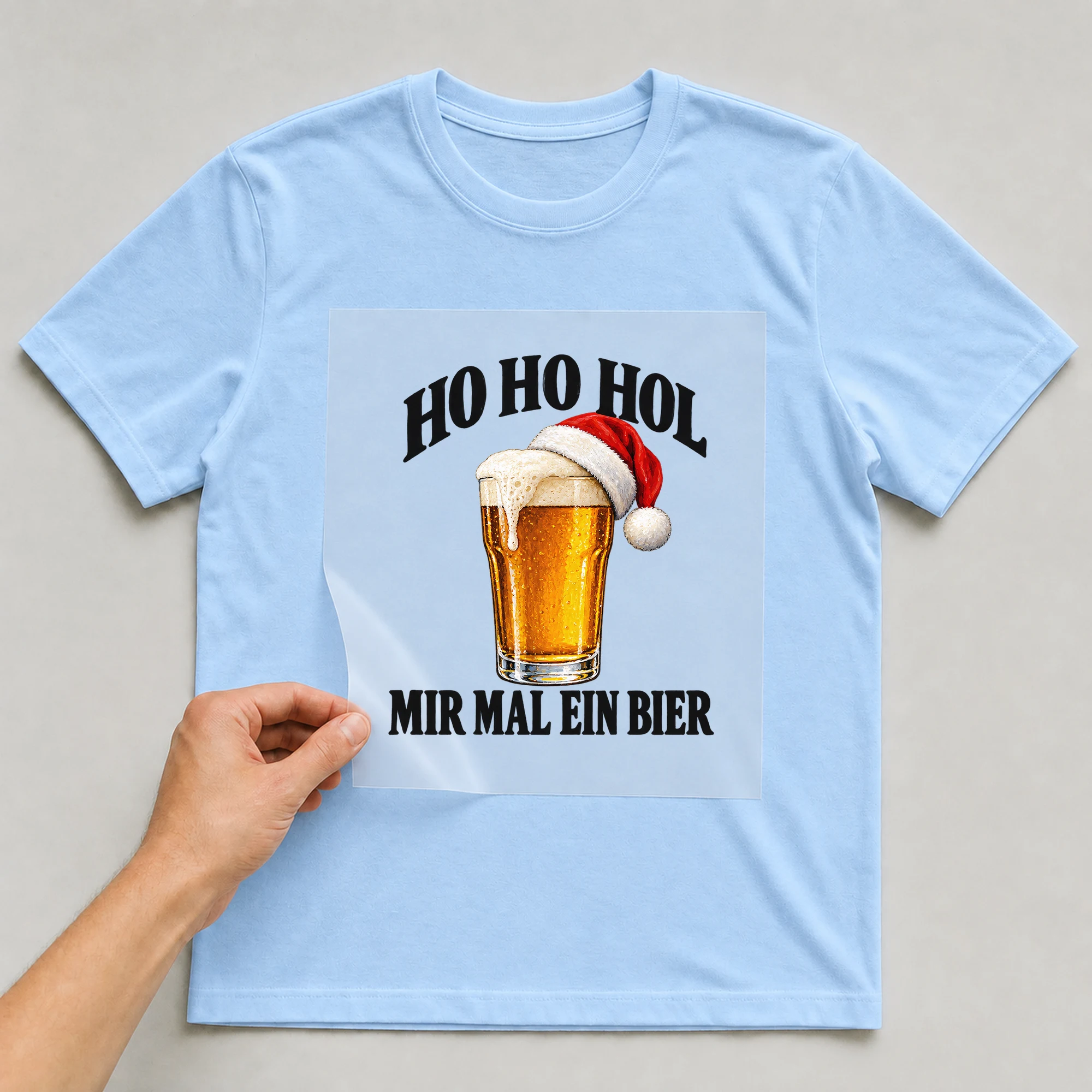 Bügelbild „Ho Ho hol mir mal ein Bier“ auf babyblauem T-Shirt, Folie wird aufgelegt