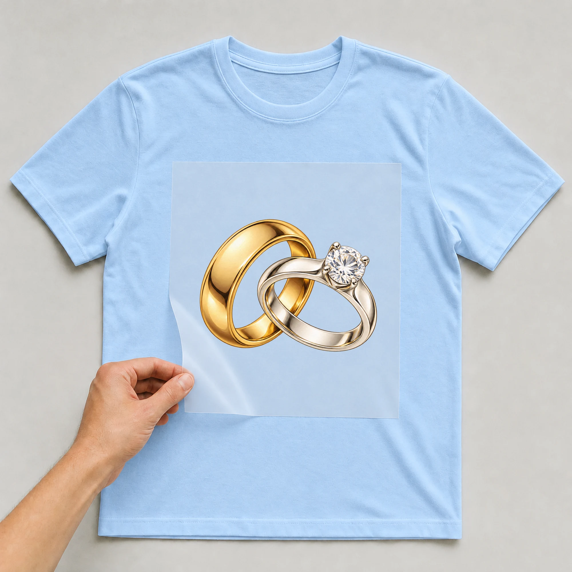 Bügelbild „Eheringe“ auf babyblauem T-Shirt, Folie wird aufgelegt