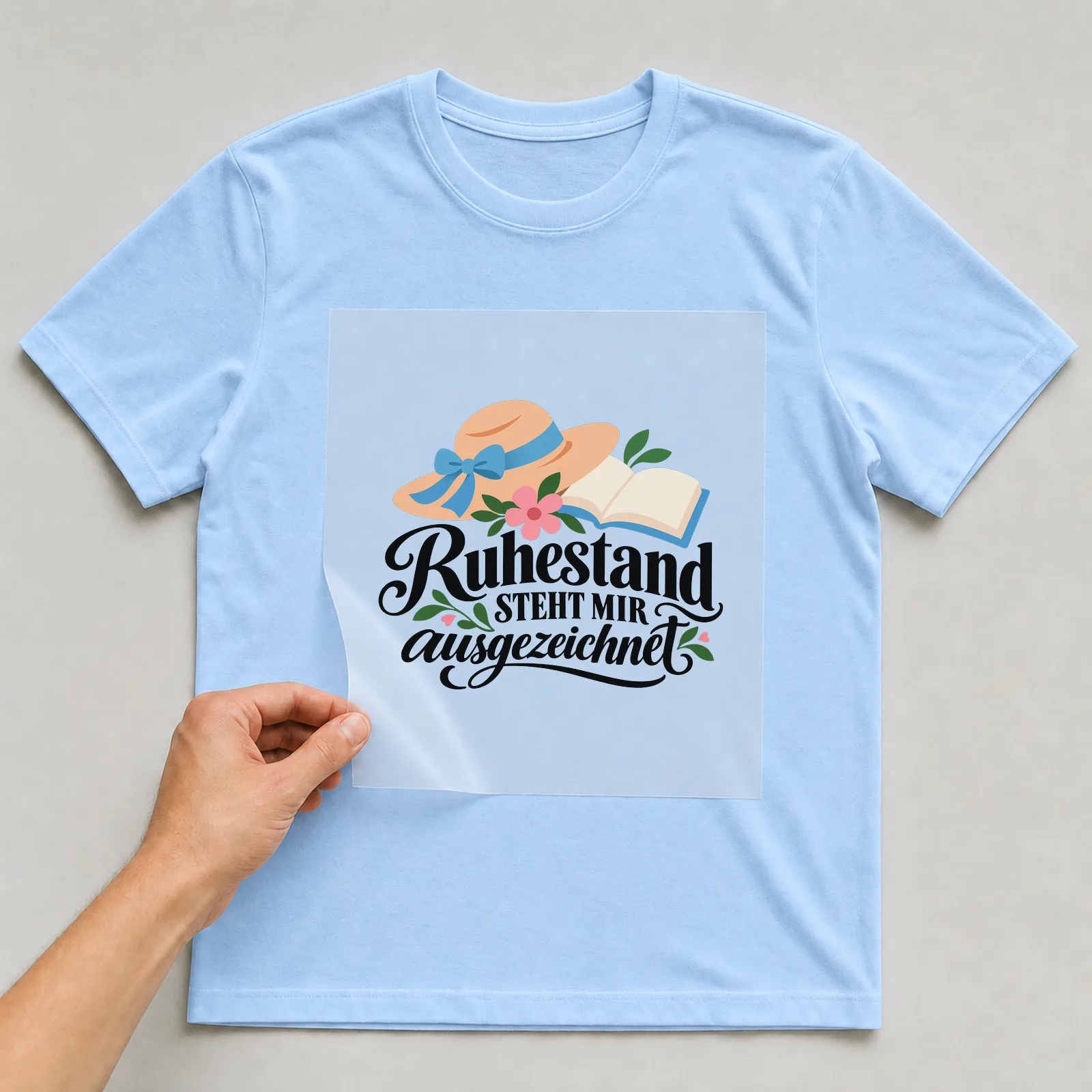 Bügelbild „Ruhestand STEHT MIR ausgezeichnet“ auf hellblauem T-Shirt, Folie wird aufgelegt