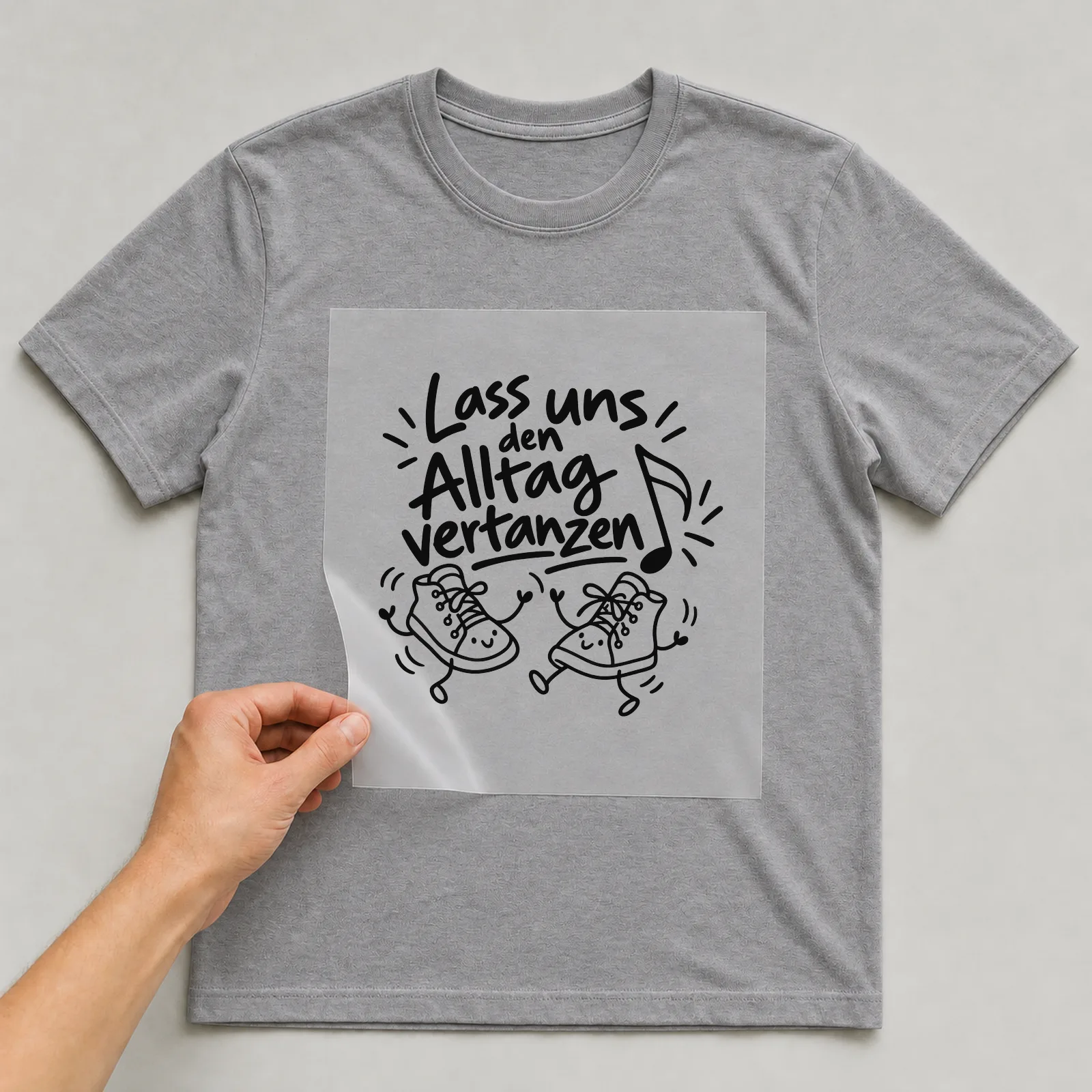 Bügelbild „Lass uns den Alltag vertanzen“ auf grauem T-Shirt, Folie wird aufgelegt