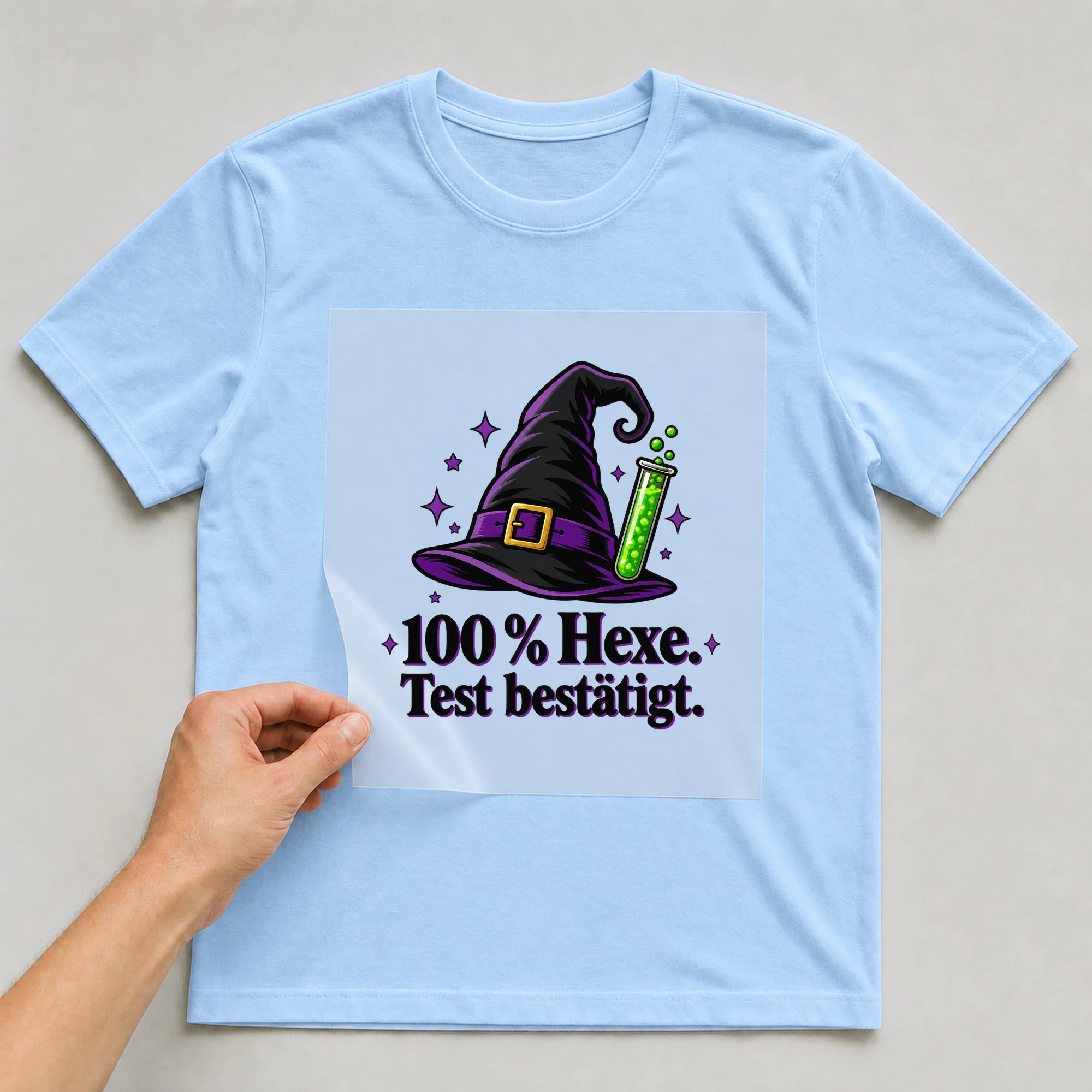 Bügelbild „100 % Hexe. Test bestätigt.“ auf babyblauem T-Shirt, Folie wird aufgelegt
