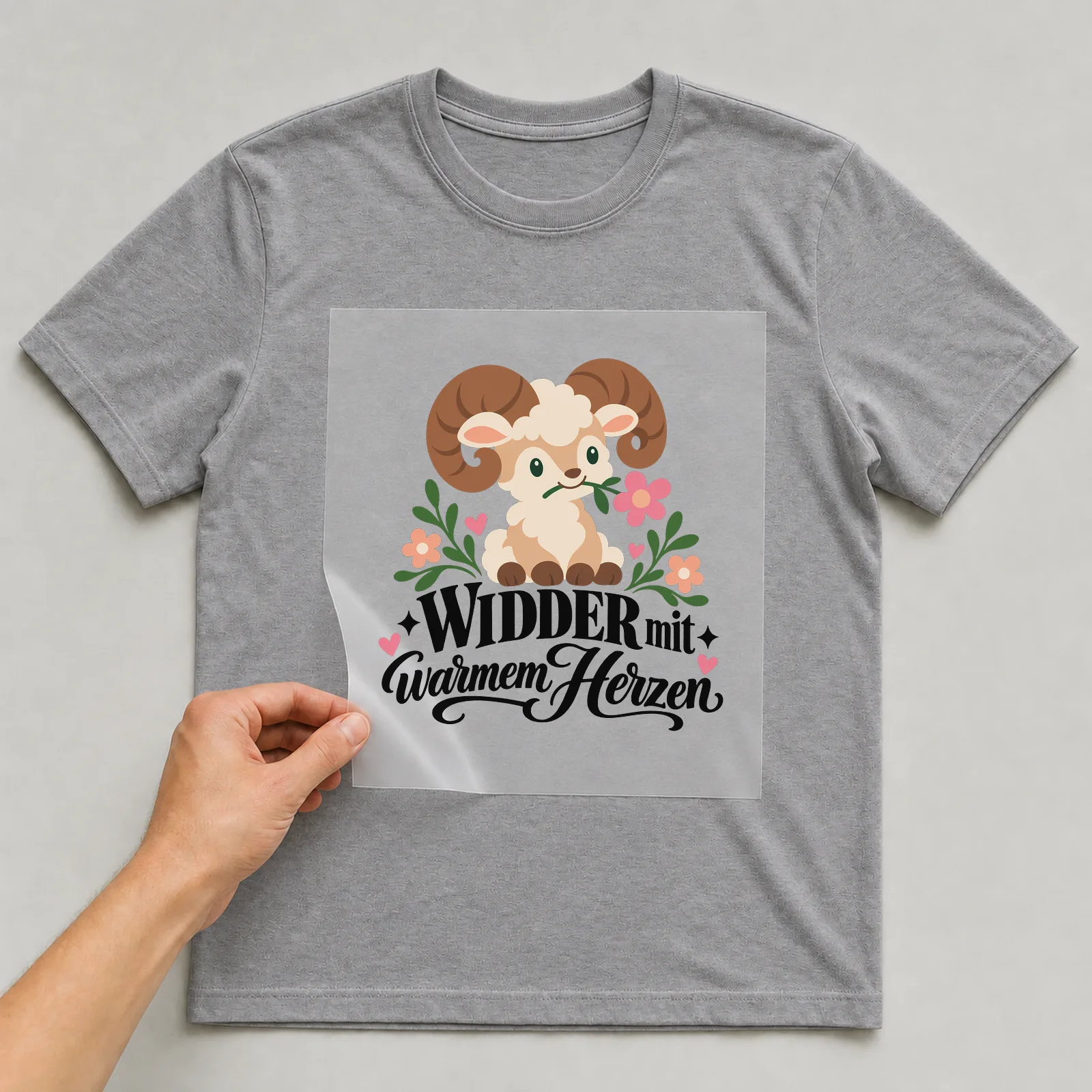 Bügelbild „Widder mit warmem Herzen“ auf grauem T-Shirt, Folie wird aufgelegt