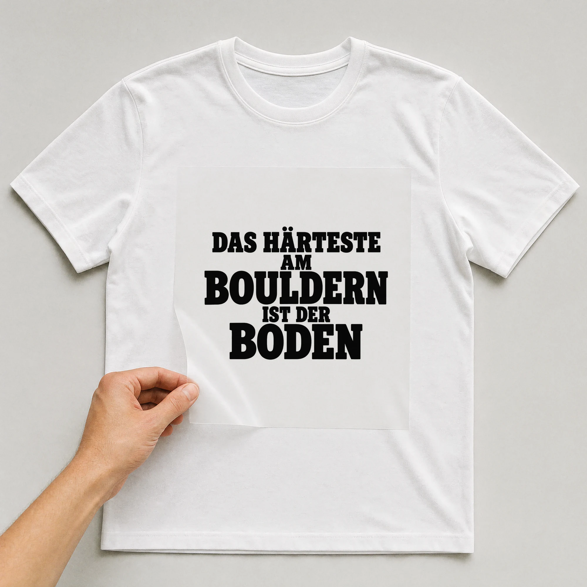 Bügelbild „Das härteste am Bouldern ist der Boden“ auf weißem T-Shirt, Folie wird aufgelegt