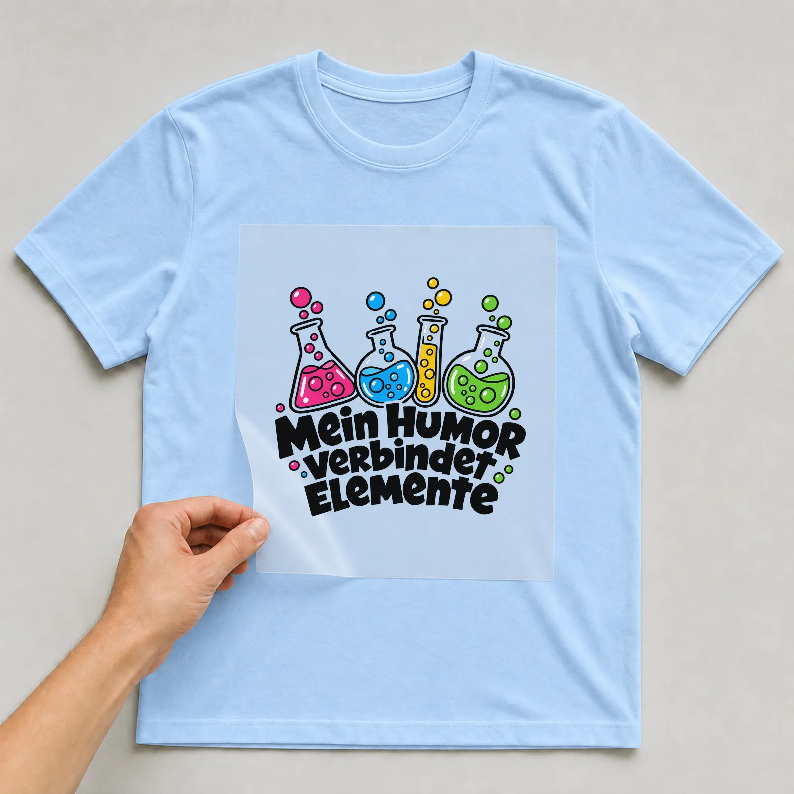 Bügelbild „Mein Humor verbindet Elemente“ auf hellblauem T-Shirt, Folie wird aufgelegt