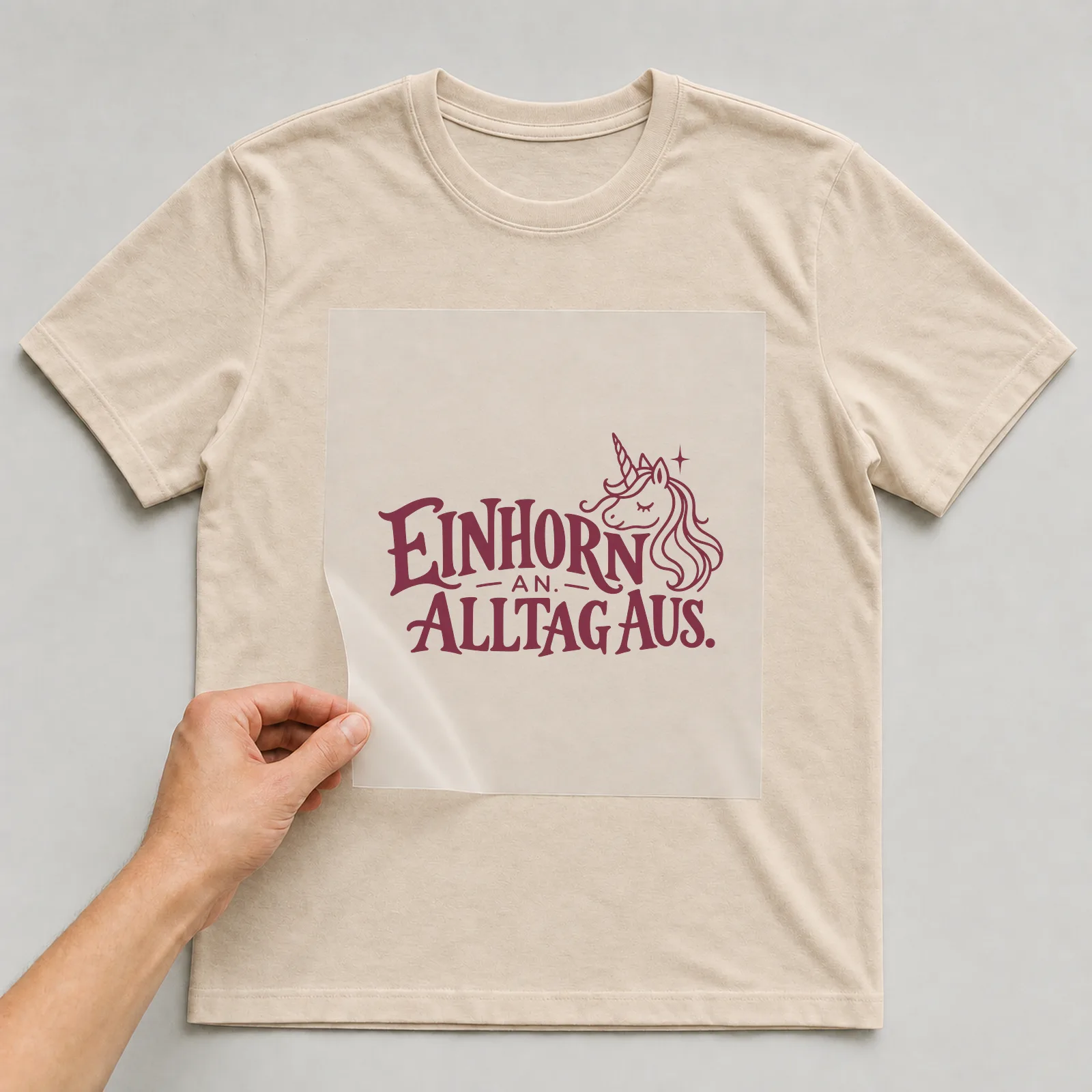 Bügelbild „Einhorn an. Alltag aus.“ auf beigem T-Shirt, Folie wird aufgelegt