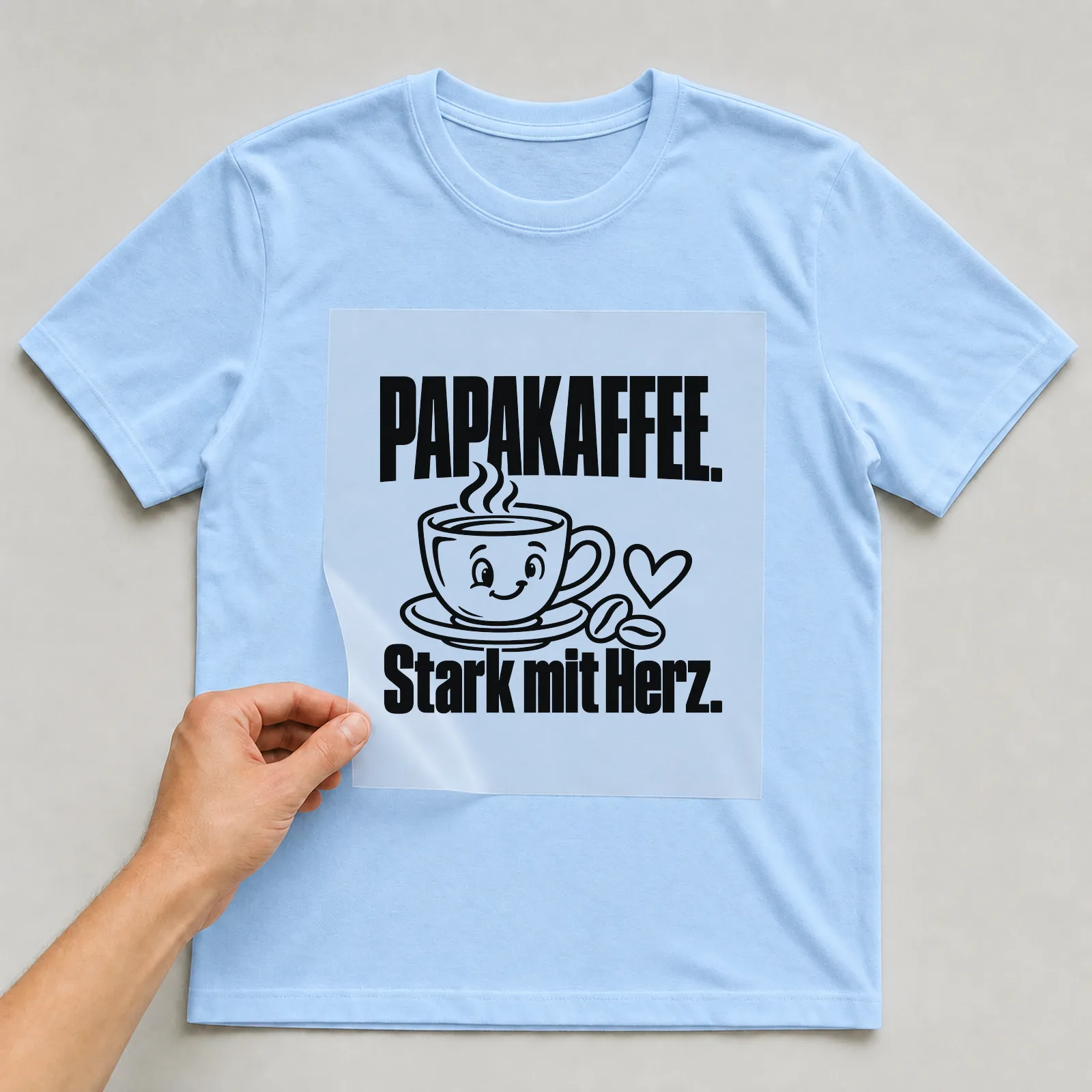 Bügelbild „Papakaffee. Stark mit Herz.“ auf hellblauem T-Shirt, Folie wird aufgelegt