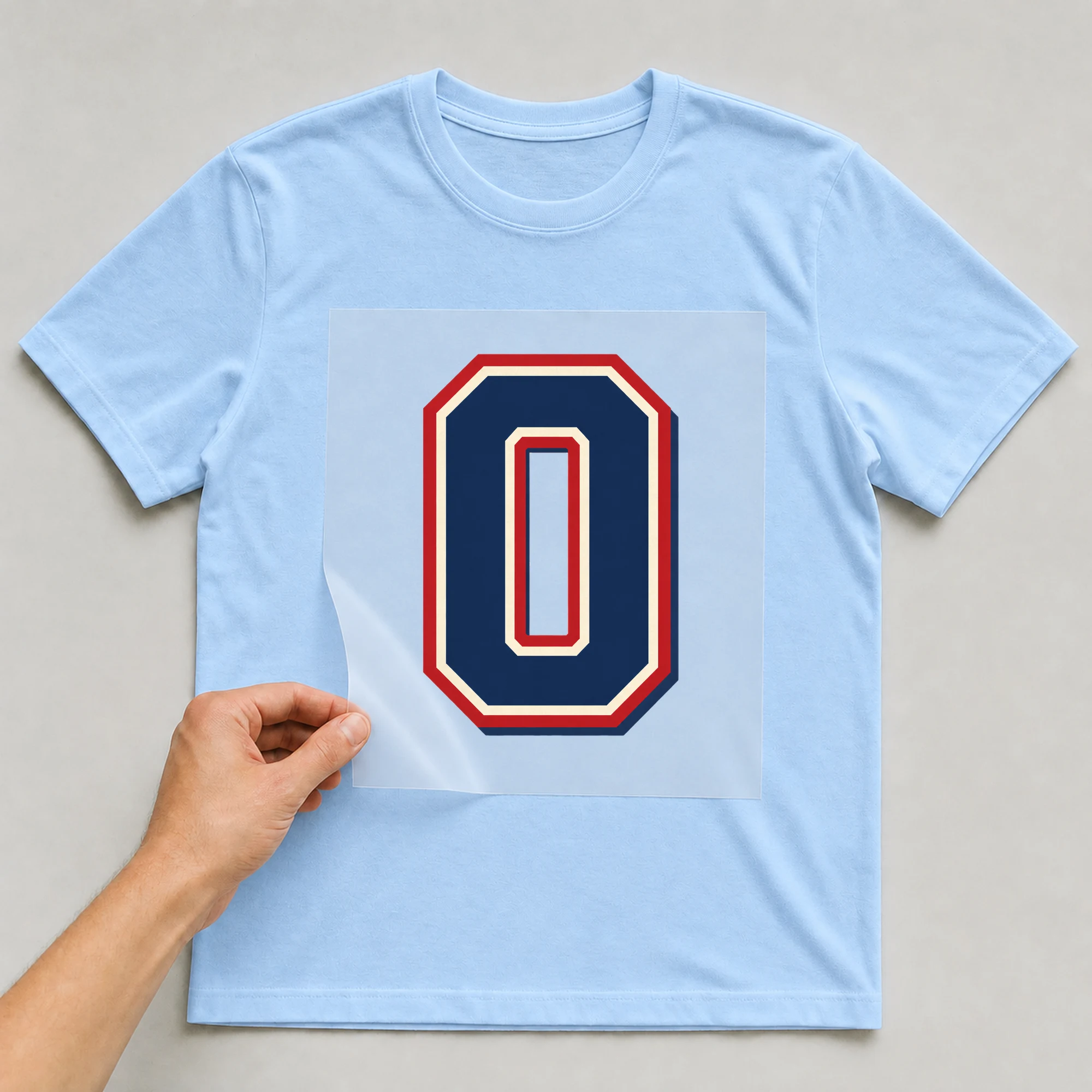Bügelbild „Zahl 0 im Retro-College-Stil“ auf babyblauem T-Shirt, Folie wird aufgelegt