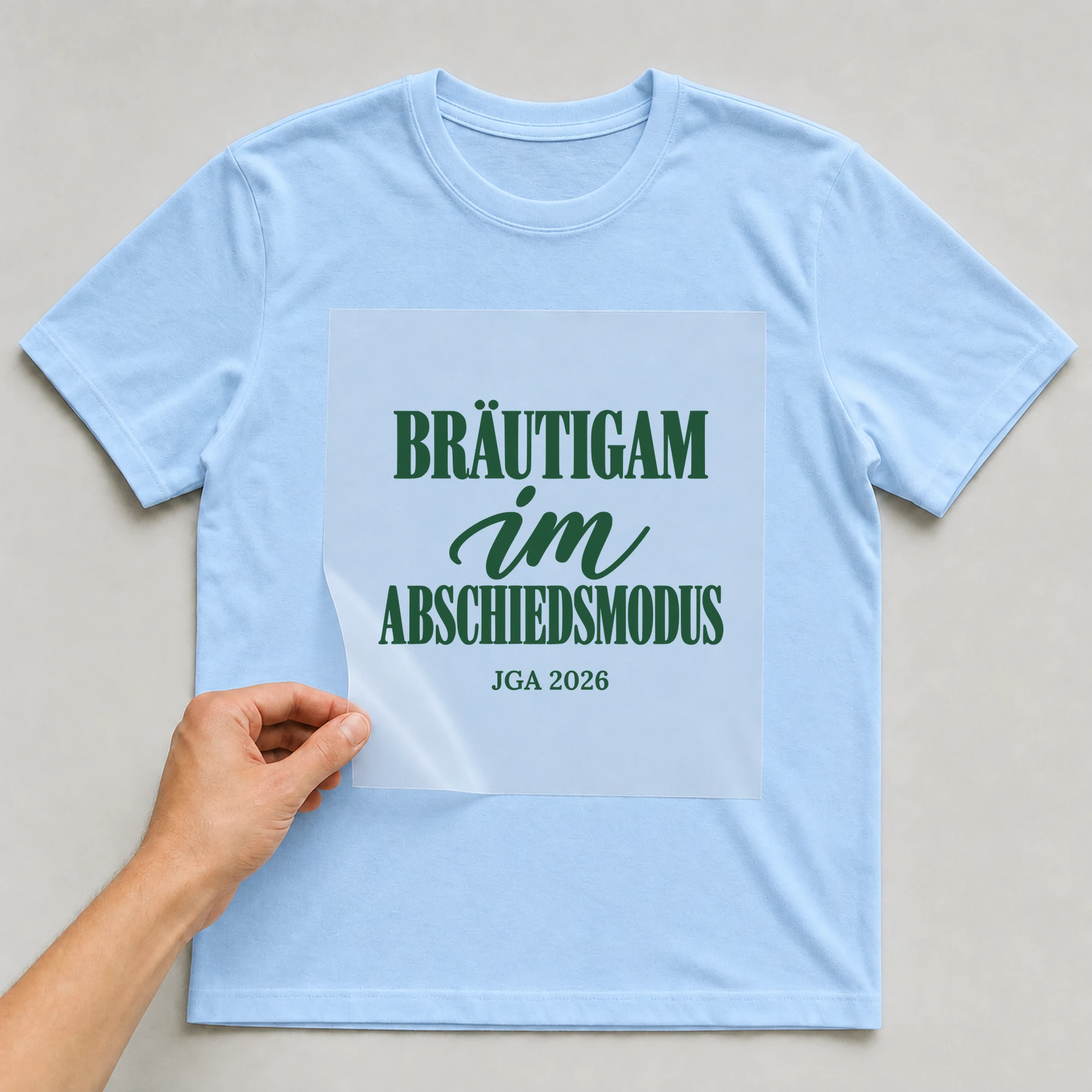 Bügelbild Bräutigam im Abschiedsmodus mit Jahr auf hellblauem T-Shirt, Folie wird aufgelegt