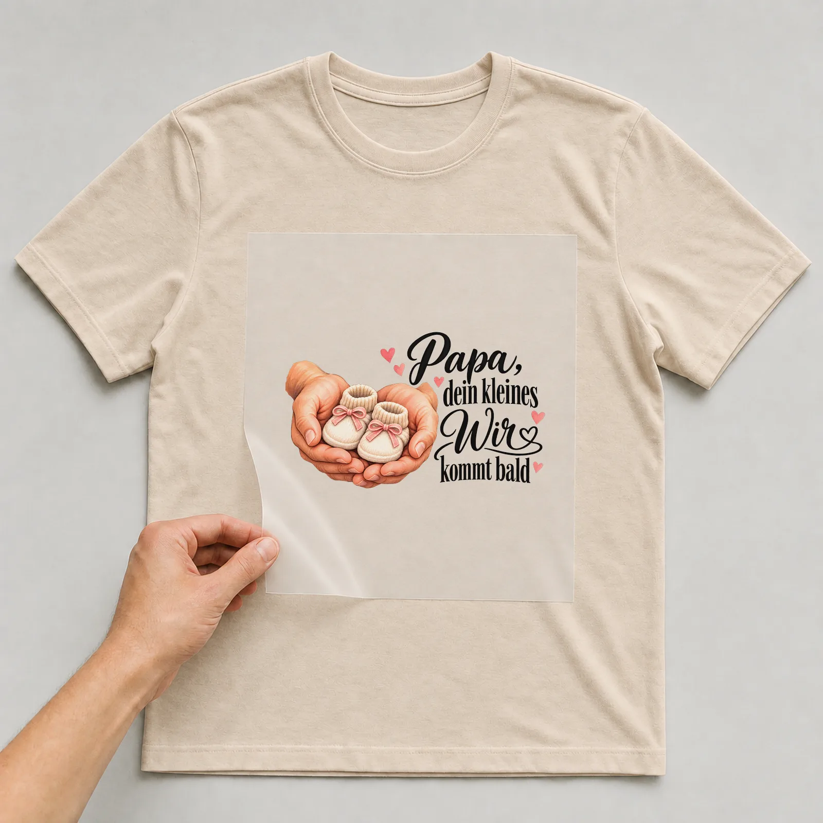 Bügelbild „Papa, dein kleines Wir kommt bald“ auf beigem T-Shirt, Folie wird aufgelegt