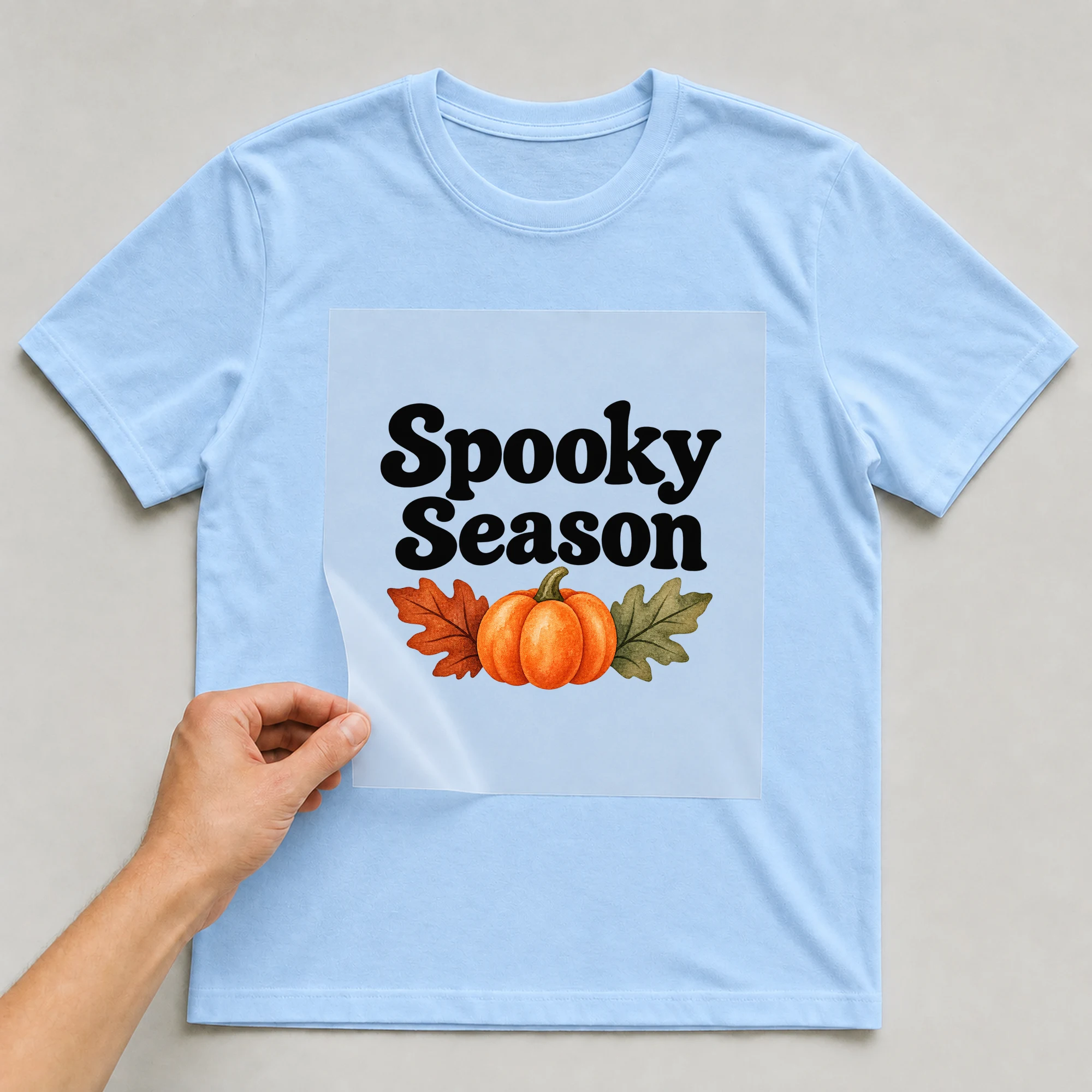 Bügelbild „Spooky Season“ auf babyblauem T-Shirt, Folie wird aufgelegt