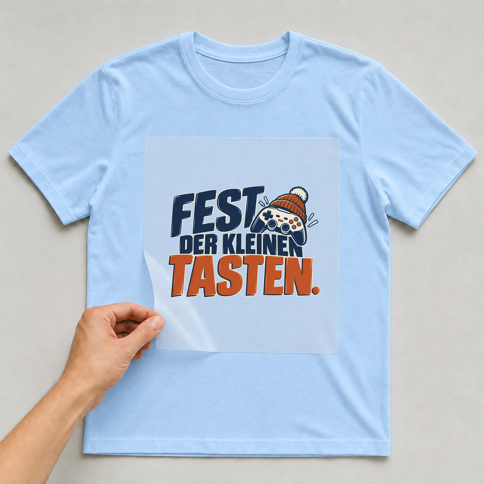 Bügelbild „Fest der Kleinen tasten“ auf hellblauem T-Shirt, Folie wird aufgelegt
