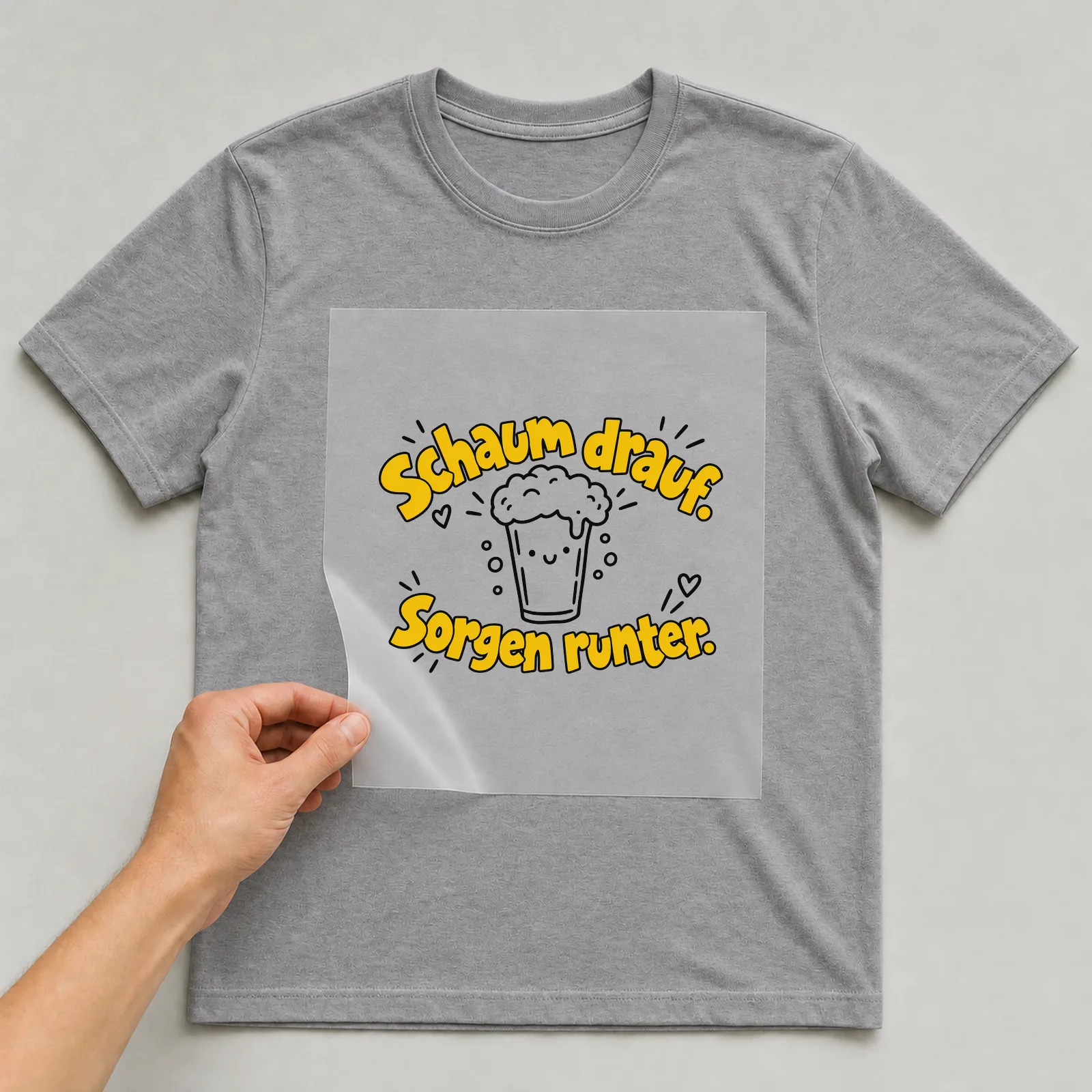 Bügelbild „Schaum drauf. Sorgen runter.“ auf grauem T-Shirt, Folie wird aufgelegt