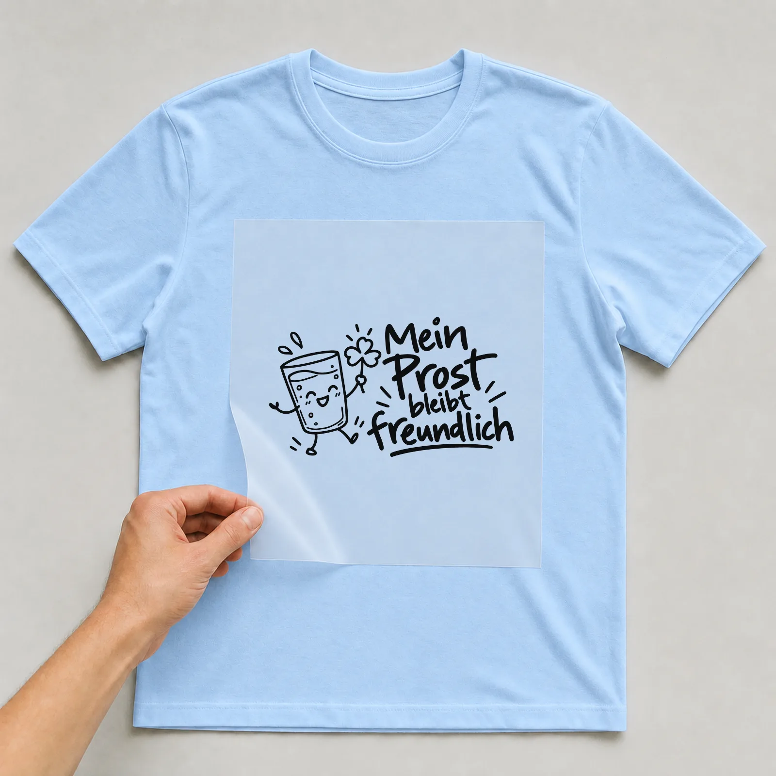 Bügelbild „Mein Prost bleibt freundlich“ auf hellblauem T-Shirt, Folie wird aufgelegt