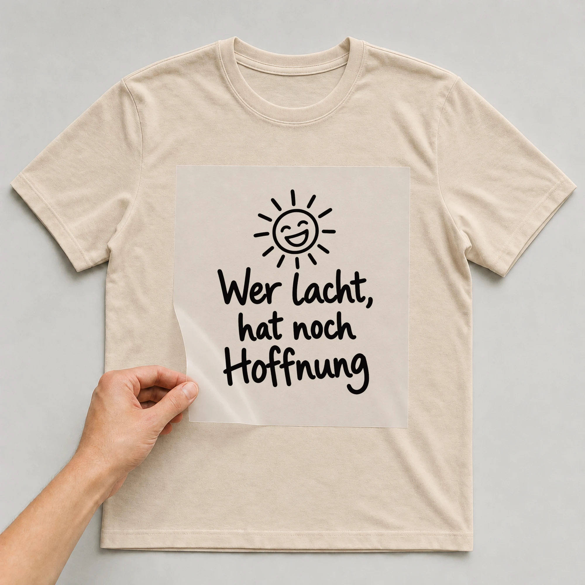 Bügelbild „Wer lacht, hat noch Hoffnung“ auf beigem T-Shirt, Folie wird aufgelegt