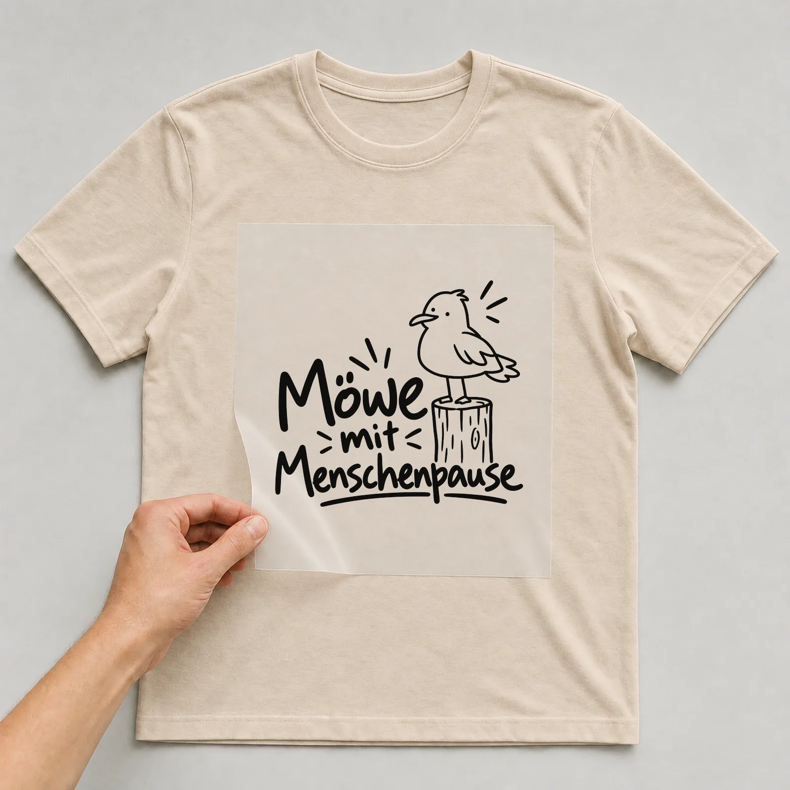 Bügelbild „Möwe mit Menschenpause“ auf beigem T-Shirt, Folie wird aufgelegt