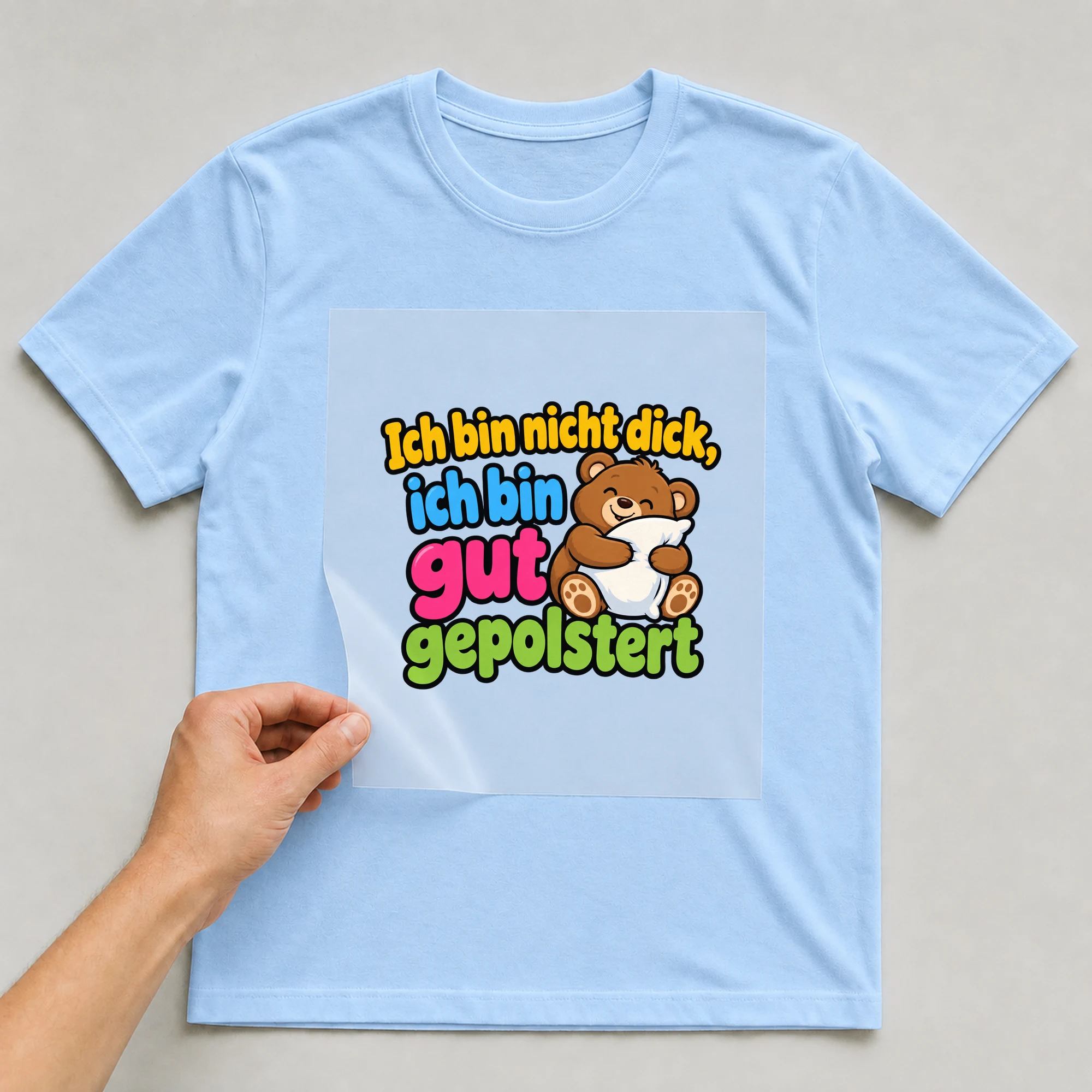 Bügelbild „Ich bin nicht dick, ich bin gut gepolstert“ auf babyblauem T-Shirt, Folie wird aufgelegt