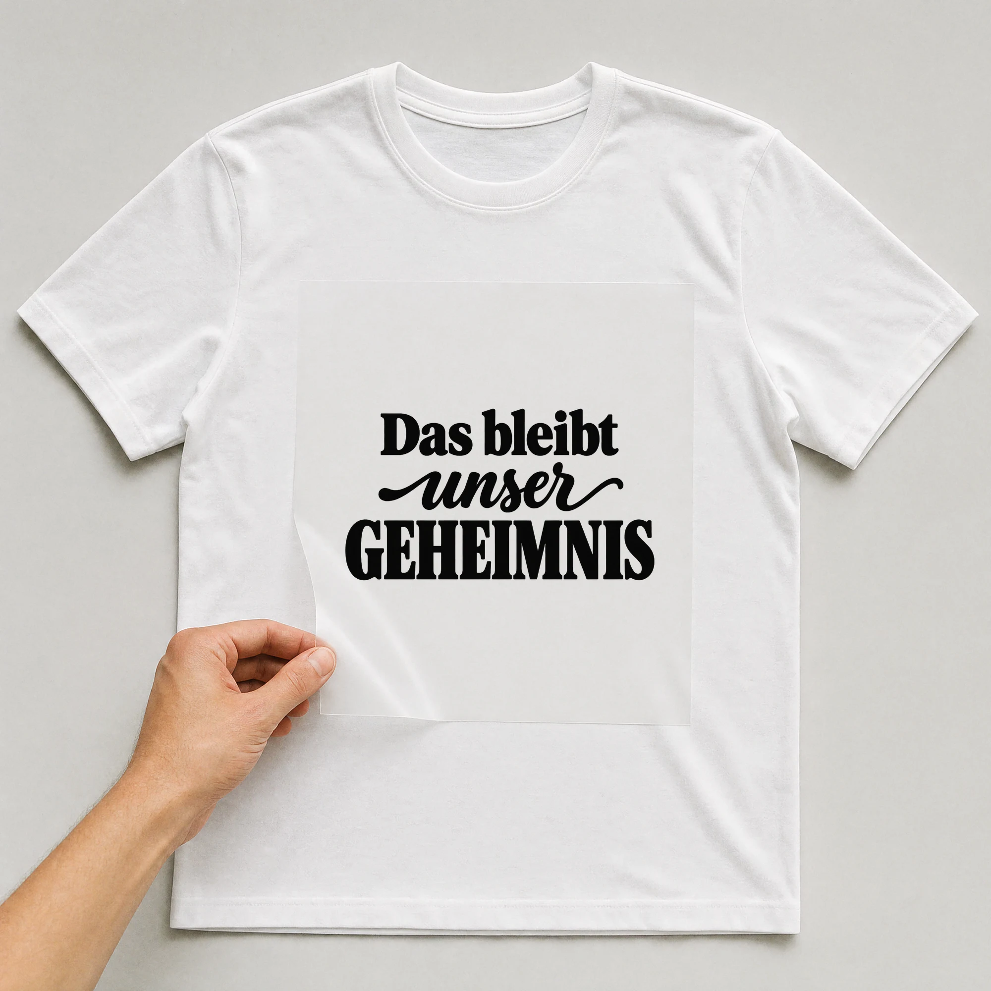 Bügelbild „Das bleibt unser Geheimnis“ auf weißem T-Shirt, Folie wird aufgelegt