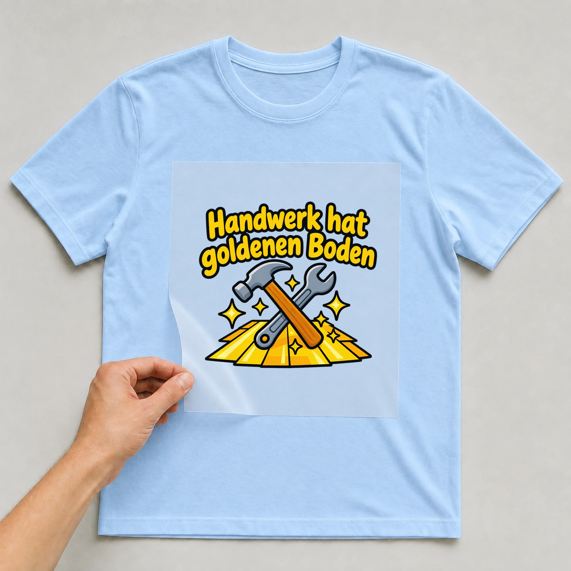 Bügelbild „Handwerk hat goldenen Boden“ auf babyblauem T-Shirt, Folie wird aufgelegt