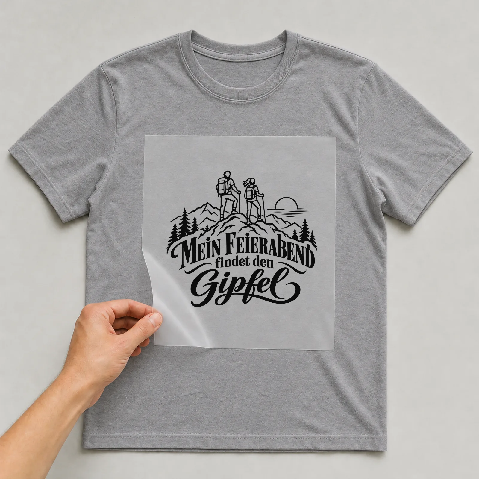 Bügelbild „MEIN FEIERABEND findet den Gipfel“ auf grauem T-Shirt, Folie wird aufgelegt