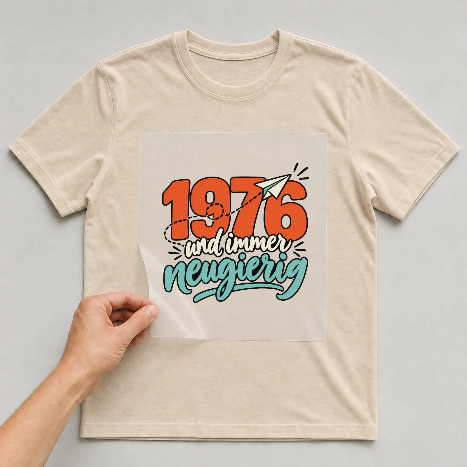 Bügelbild „1976 und immer neugierig“ auf beigem T-Shirt, Folie wird aufgelegt