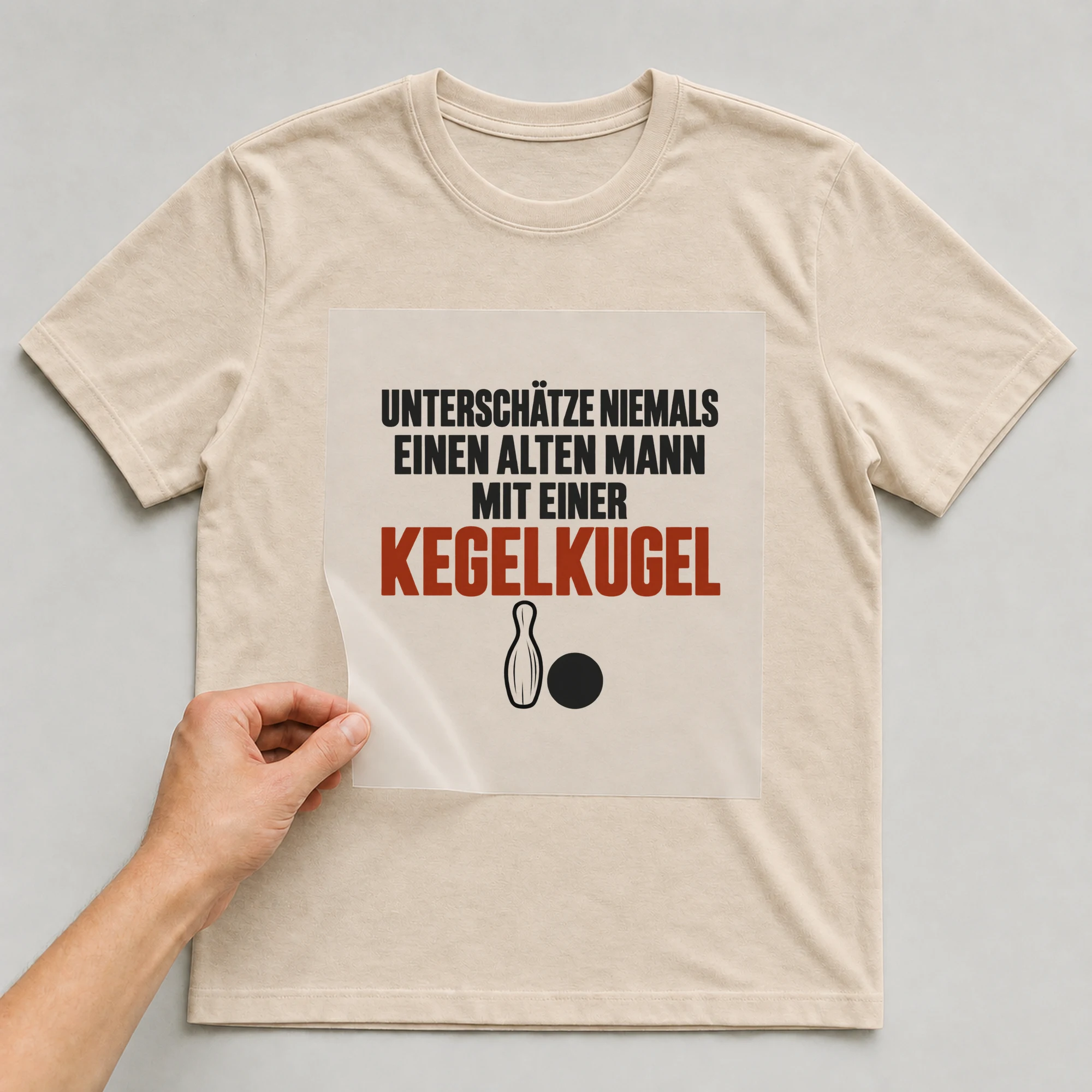 Bügelbild „Unterschätze niemals einen alten Mann mit einer Kegelkugel“ auf beigem T-Shirt, Folie wird aufgelegt