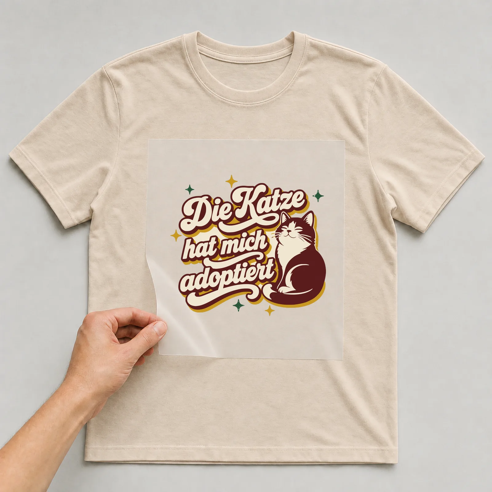 Bügelbild Die Katze hat mich adoptiert auf beigem T-Shirt, Folie wird aufgelegt