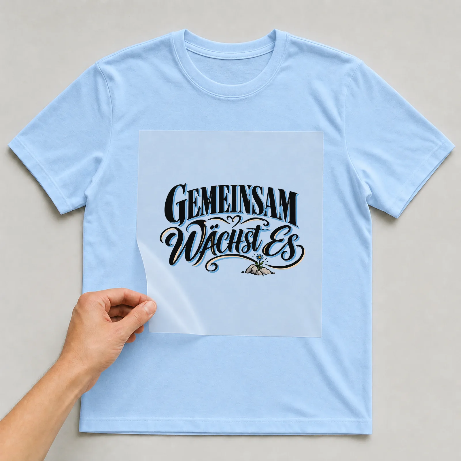 Bügelbild „Gemeinsam wächst es“ auf hellblauem T-Shirt, Folie wird aufgelegt